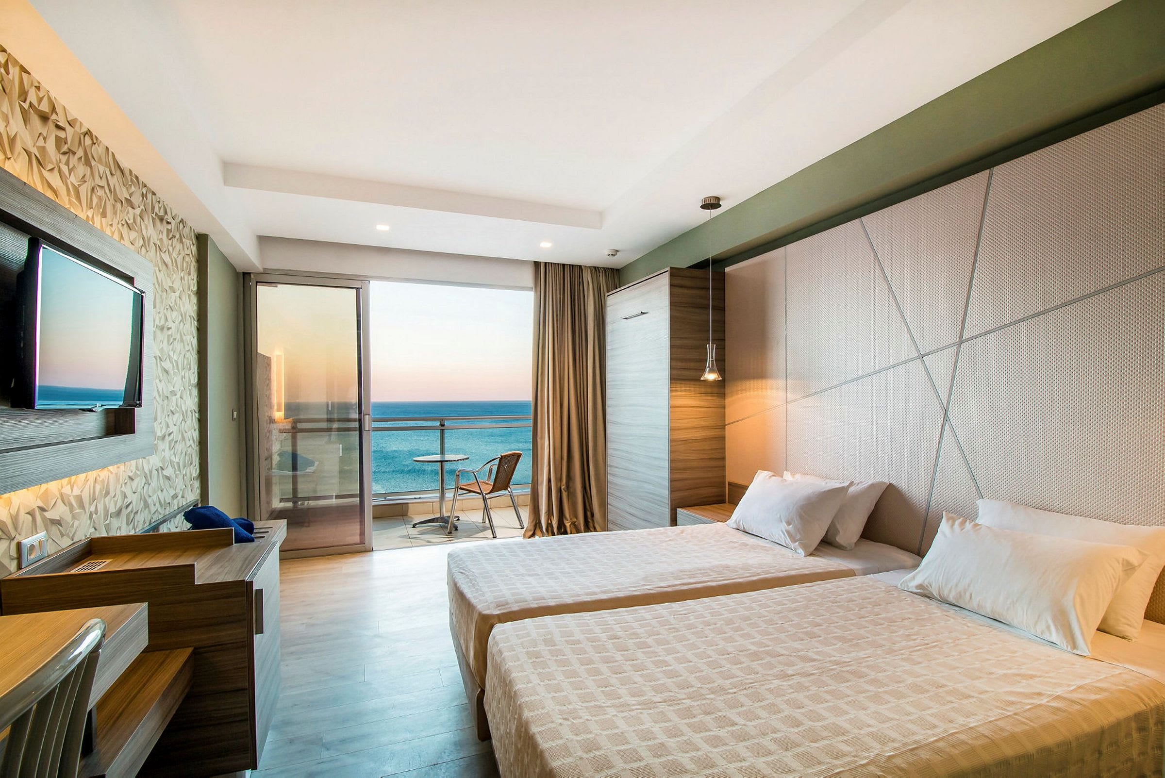 Ett hotellrum med två sängar, en TV, ett skrivbord och en balkong med utsikt över havet. (AI-genererad text)