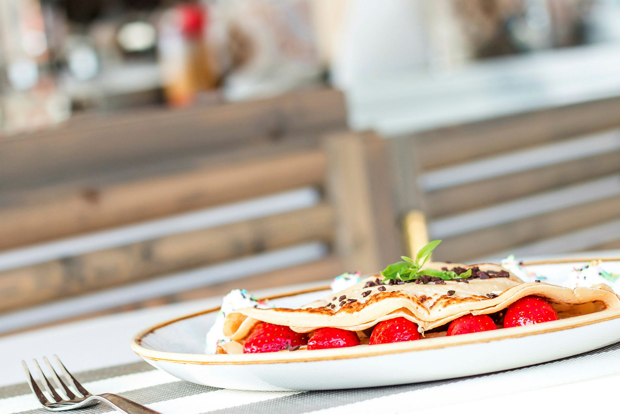 En tallrik med en dessert bestående av crepes, jordgubbar och chokladflisor. (AI-genererad text)