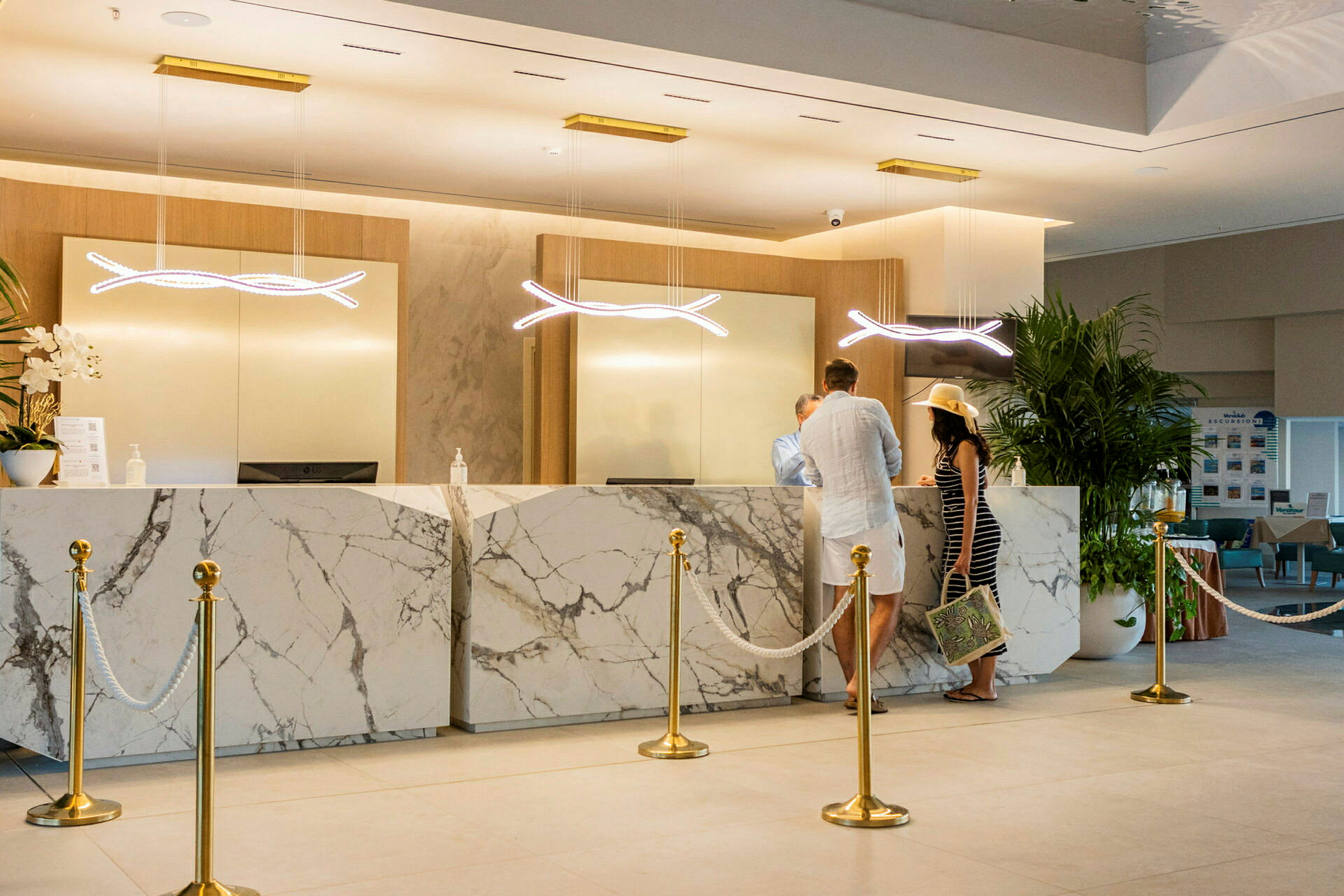 En reception med marmordisk och två personer som interagerar med personalen. (AI-genererad text)