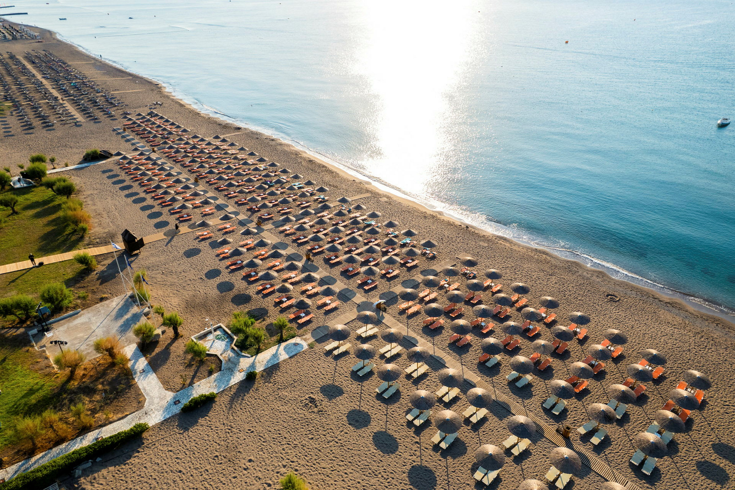 Flygfoto över en strand med solstolar och parasoller i rader vid vattnet. (AI-genererad text)