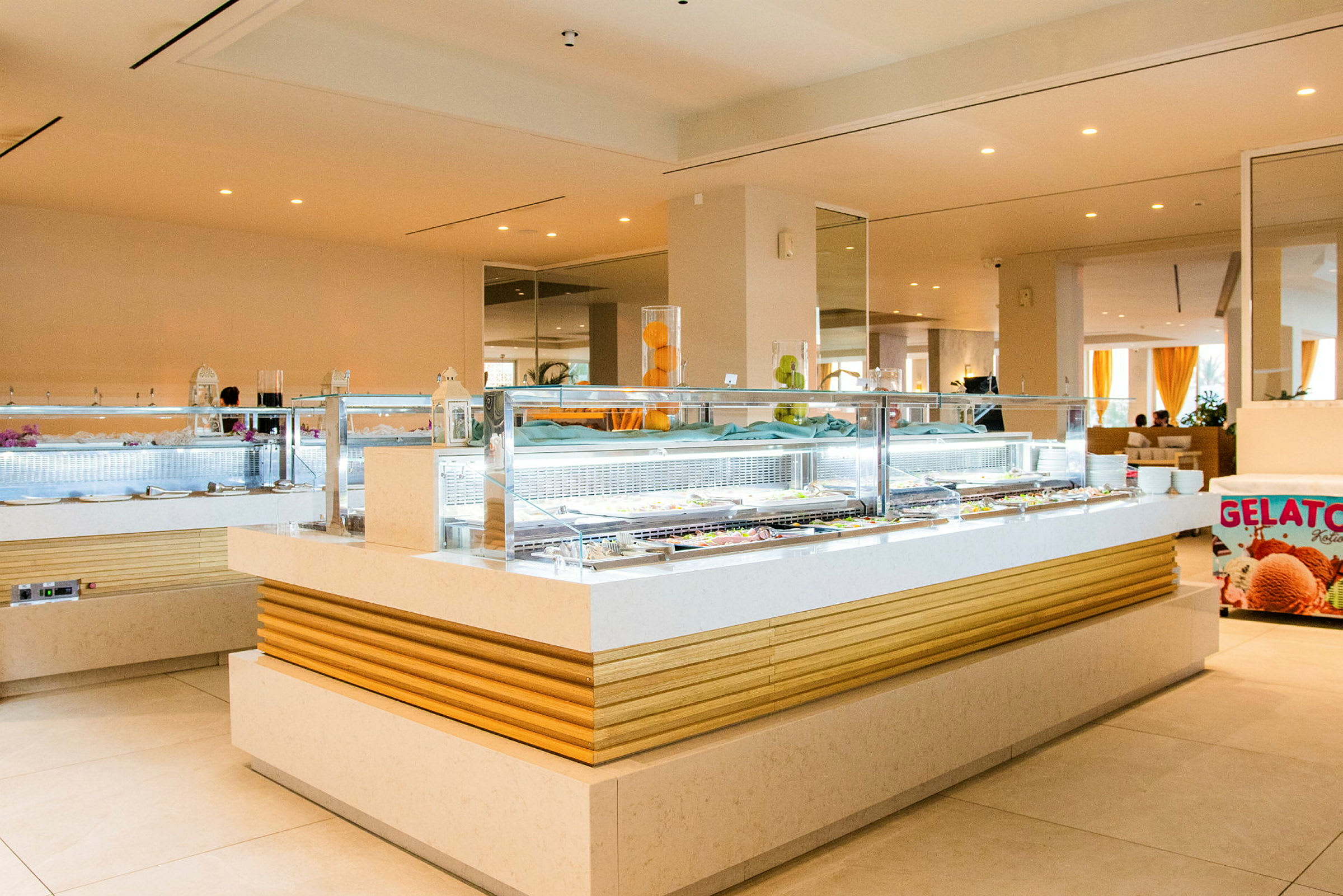 En bild av en modern bufféstation med en glasskylt som visar "Gelato" och en glasyta med olika matalternativ. (AI-genererad text)