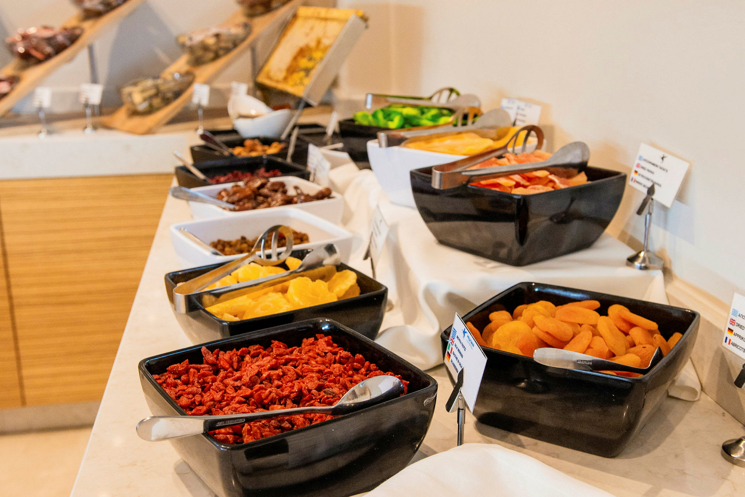 En buffé med olika torkade frukter och färska livsmedel i svarta och vita skålar på ett dukat bord. (AI-genererad text)