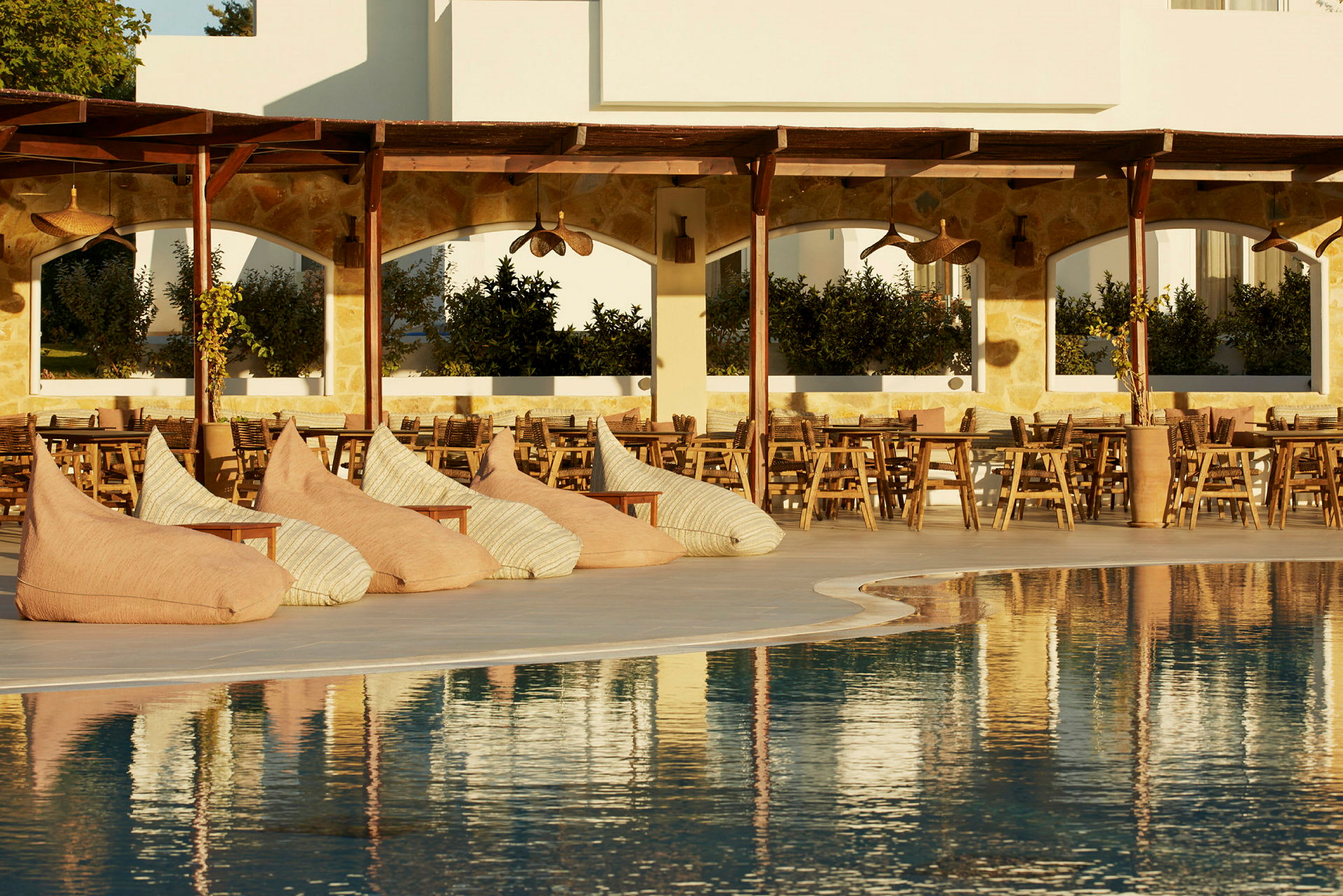 Flera sittsäckar och träbord vid en pool under en pergola. (AI-genererad text)