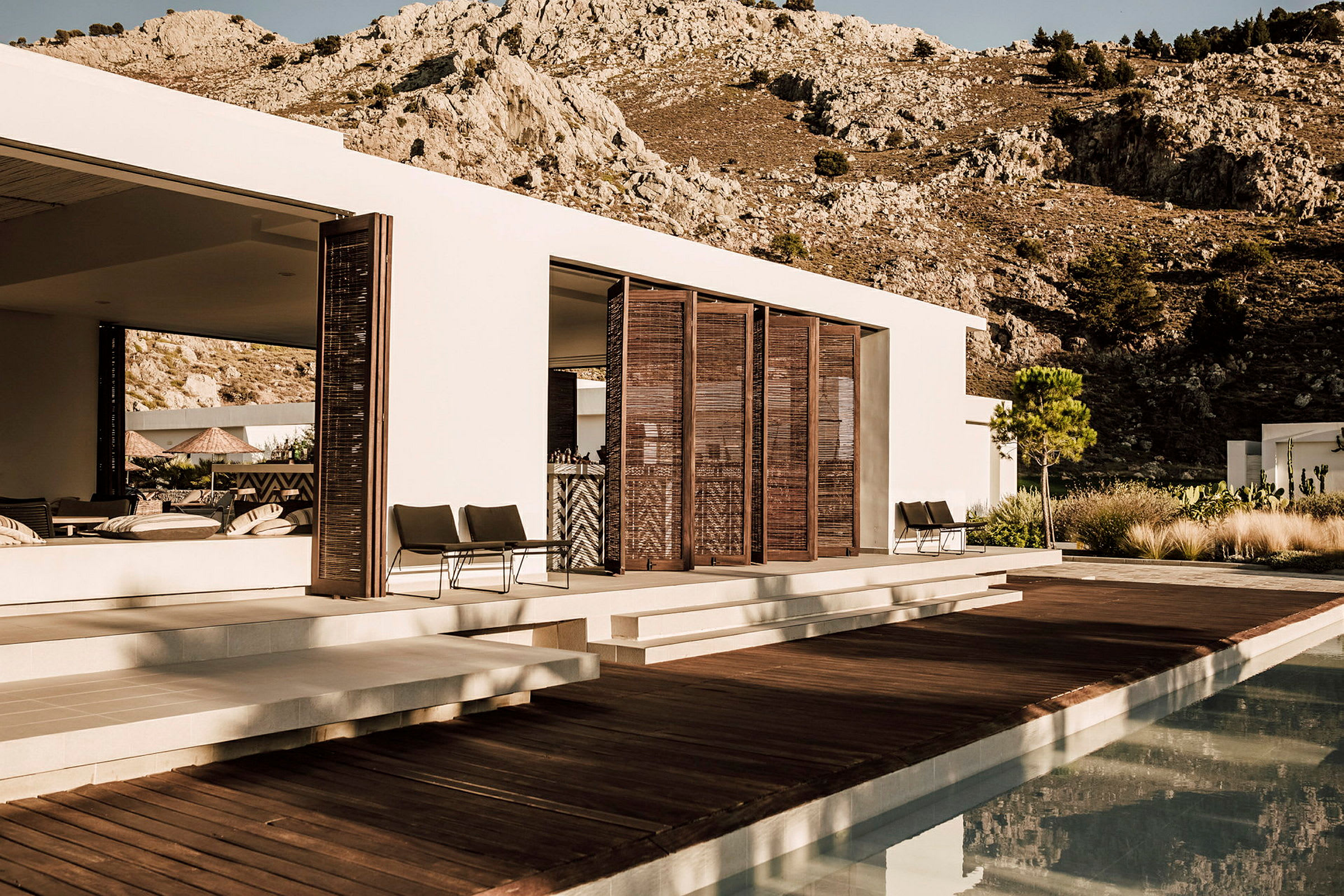 Modern villa med trätrall och pool framför bergig bakgrund. (AI-genererad text)
