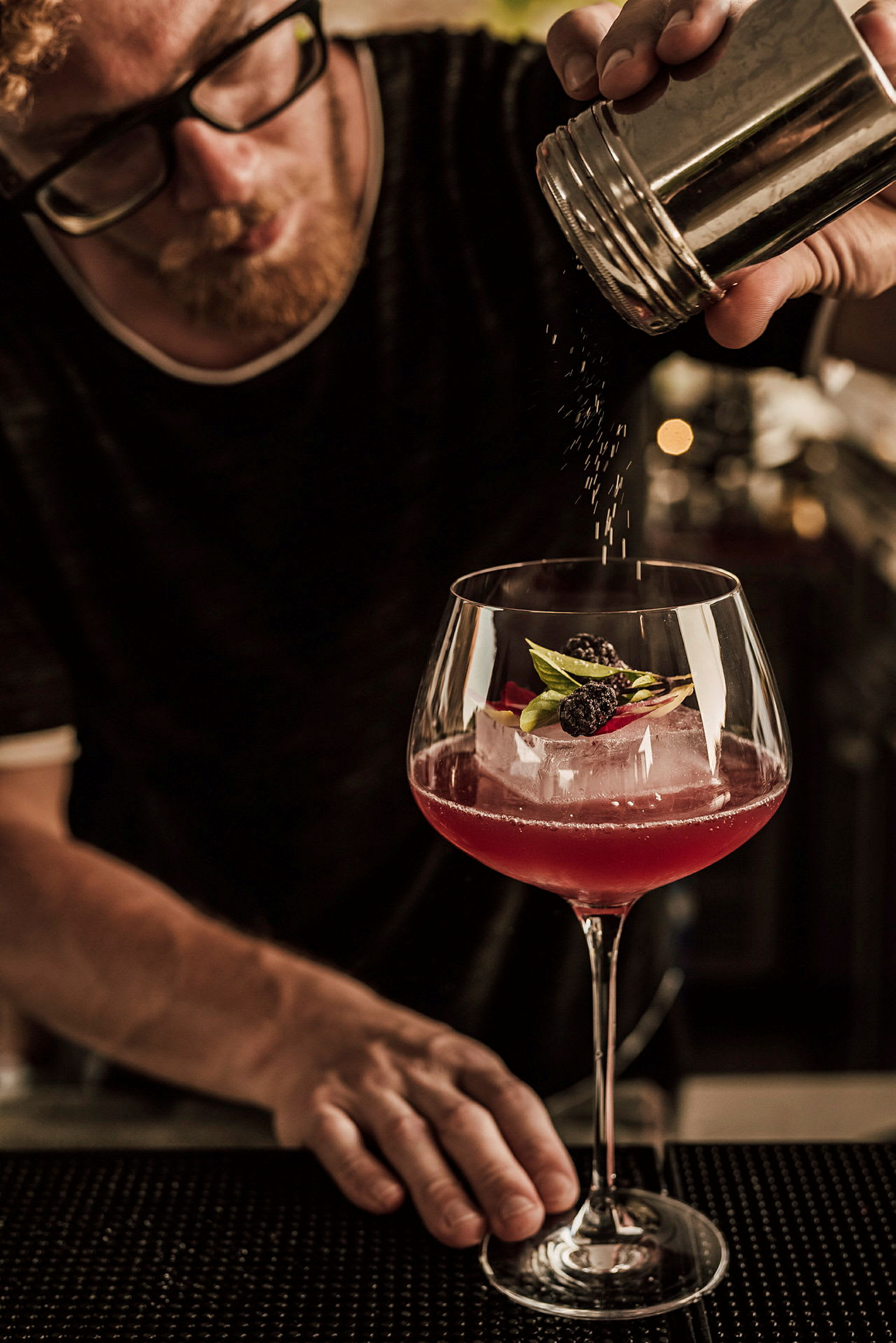 En hand strör pulver över en cocktailgarnerad med bär och blad. (AI-genererad text)