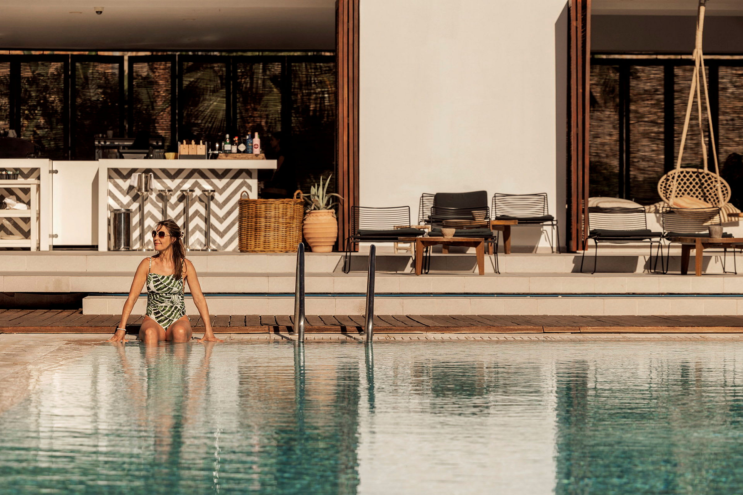 En pool framför en modern byggnad med sittmöbler och dekorationer. (AI-genererad text)