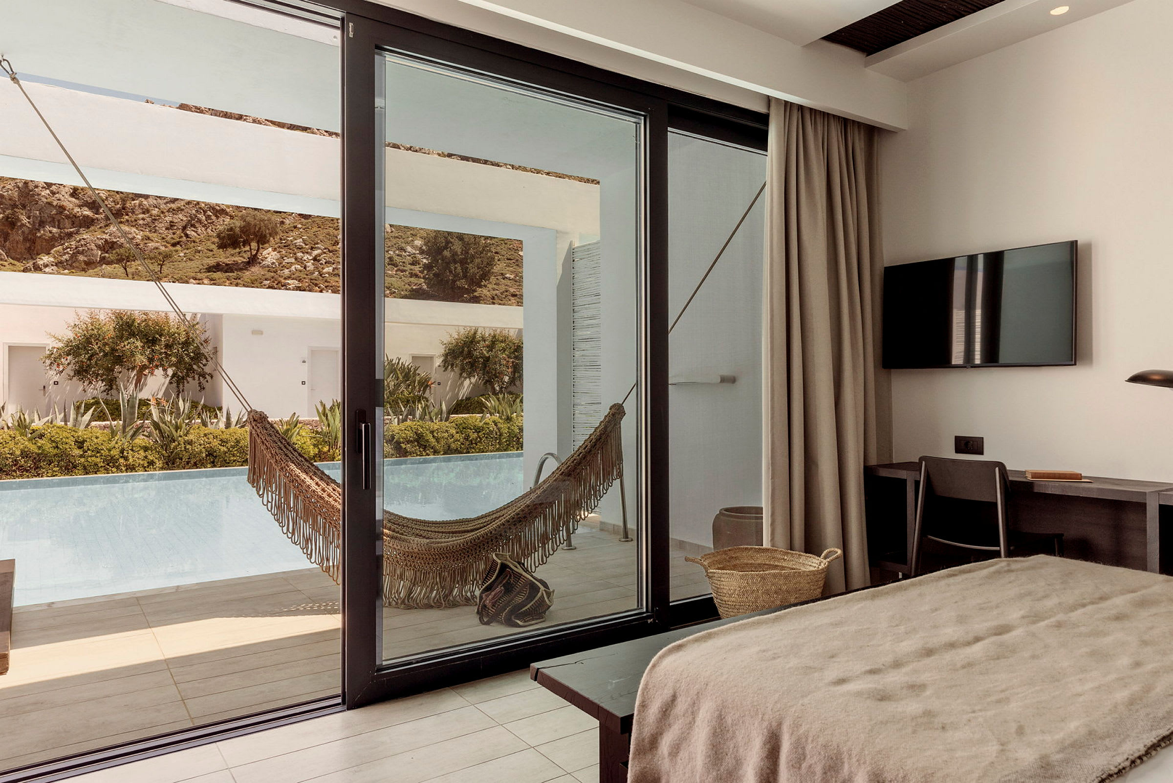 Hotellrum med utsikt mot terrass med hängmatta och pool. (AI-genererad text)