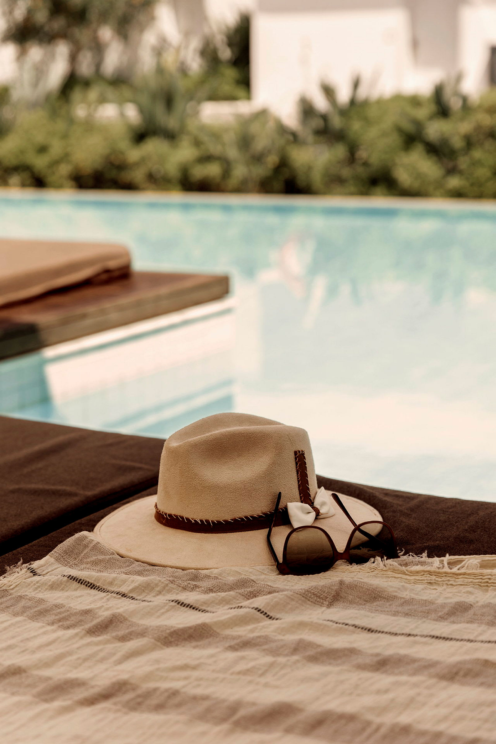 En hatt och solglasögon ligger på en solsäng vid en pool. (AI-genererad text)