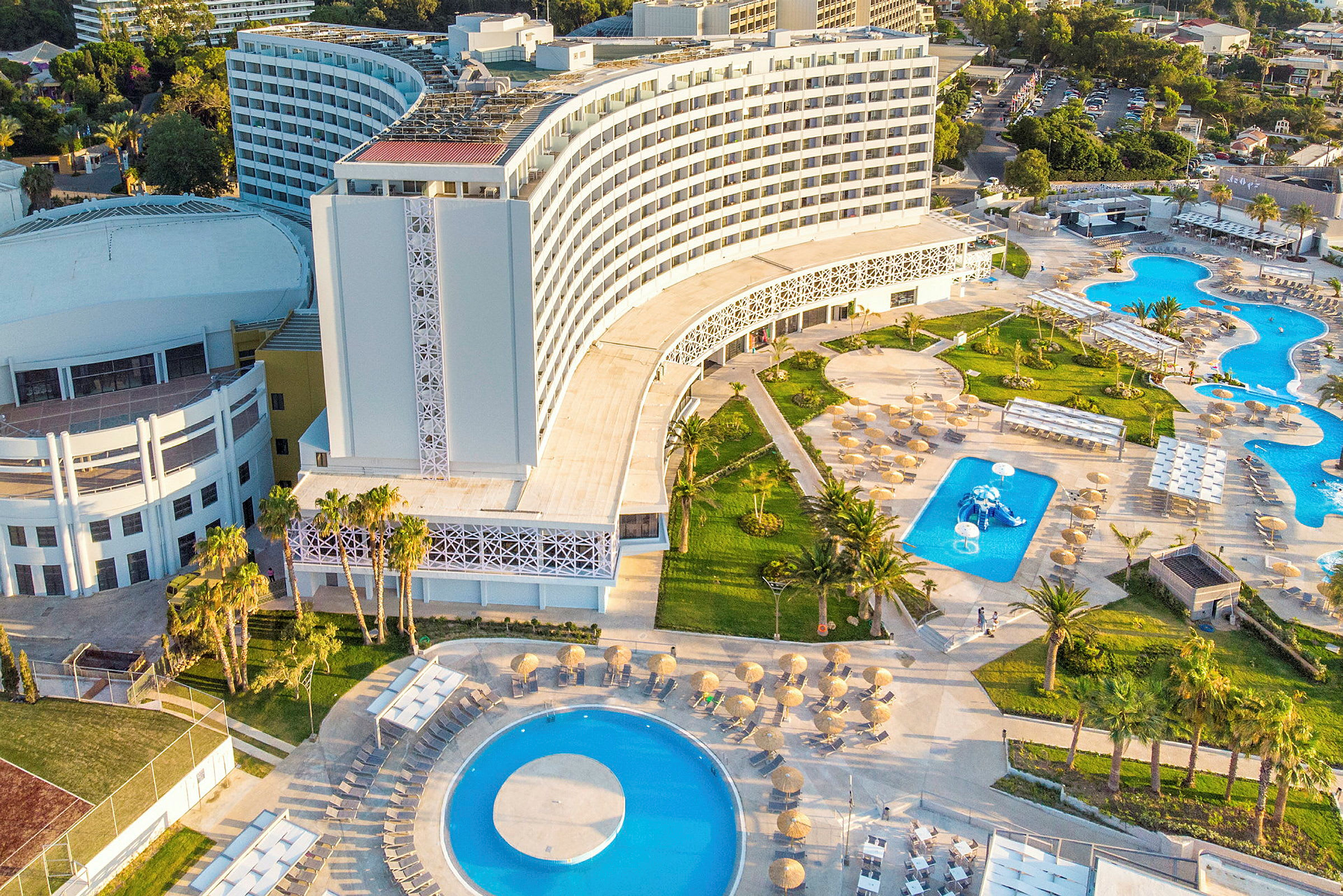 Flygvy av ett modernt hotell med pooler och grönområde. (AI-genererad text)