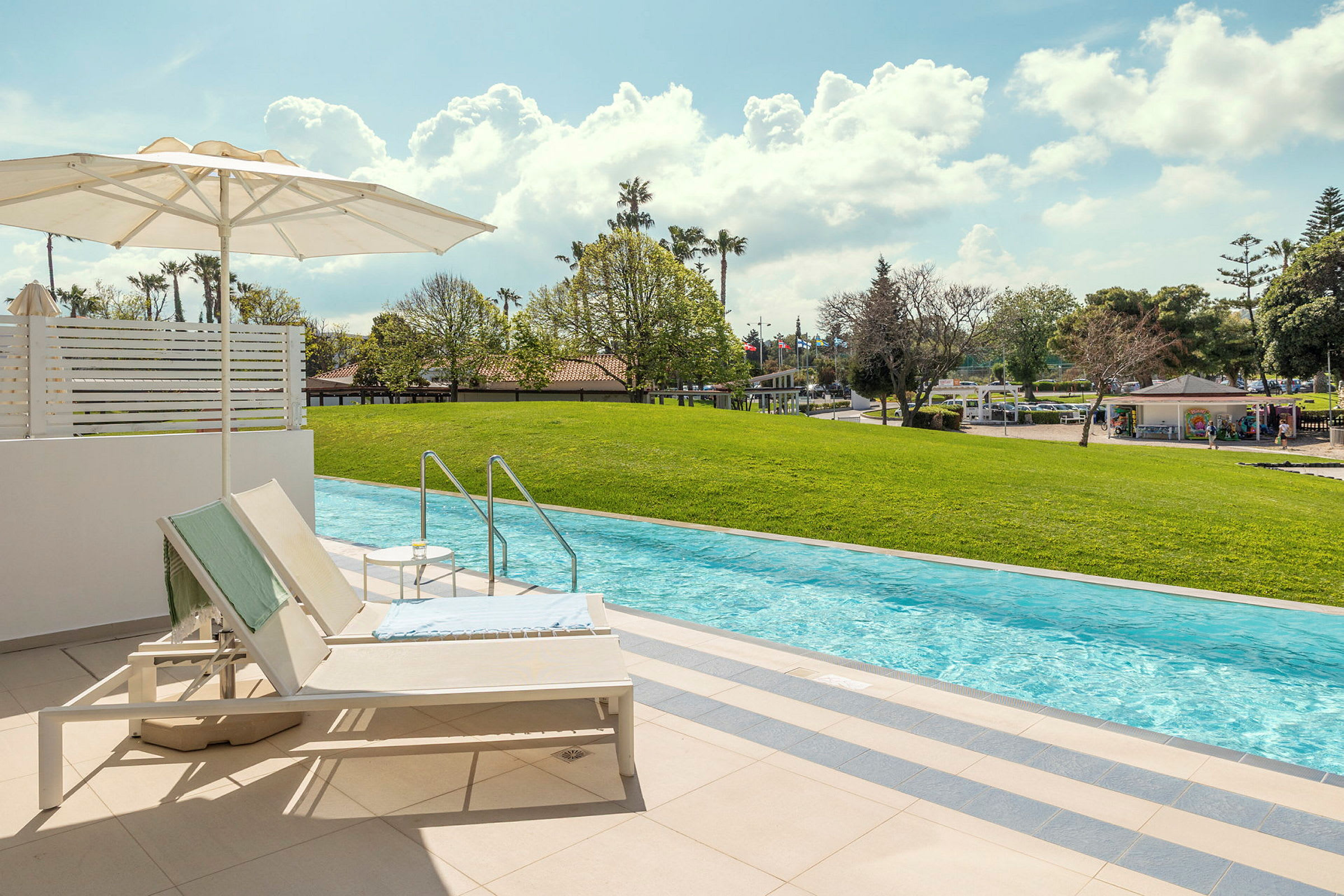 Solstolar och parasoll vid en privat pool med utsikt över en grön gräsmatta. (AI-genererad text)