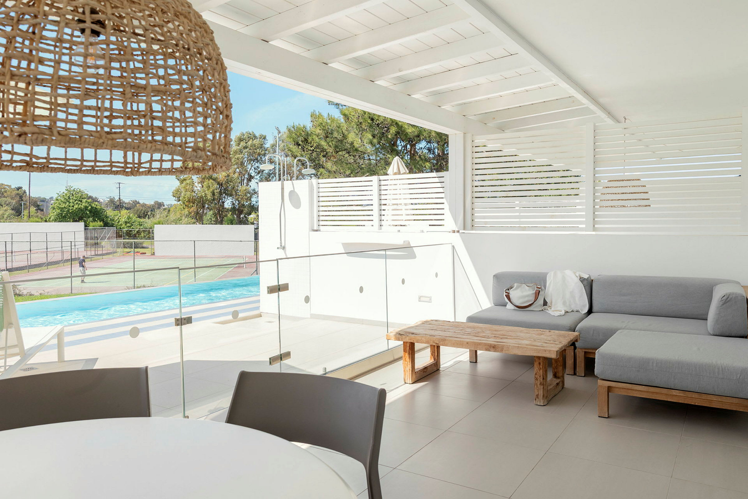 En modern uteplats med soffa, bord och utsikt över pool och tennisbanor. (AI-genererad text)