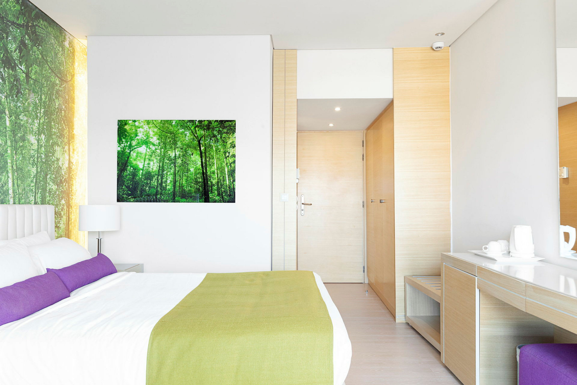 Bild på ett modernt hotellrum med en dubbelsäng, skrivbord och garderob. Väggen är dekorerad med en naturbild. (AI-genererad text)