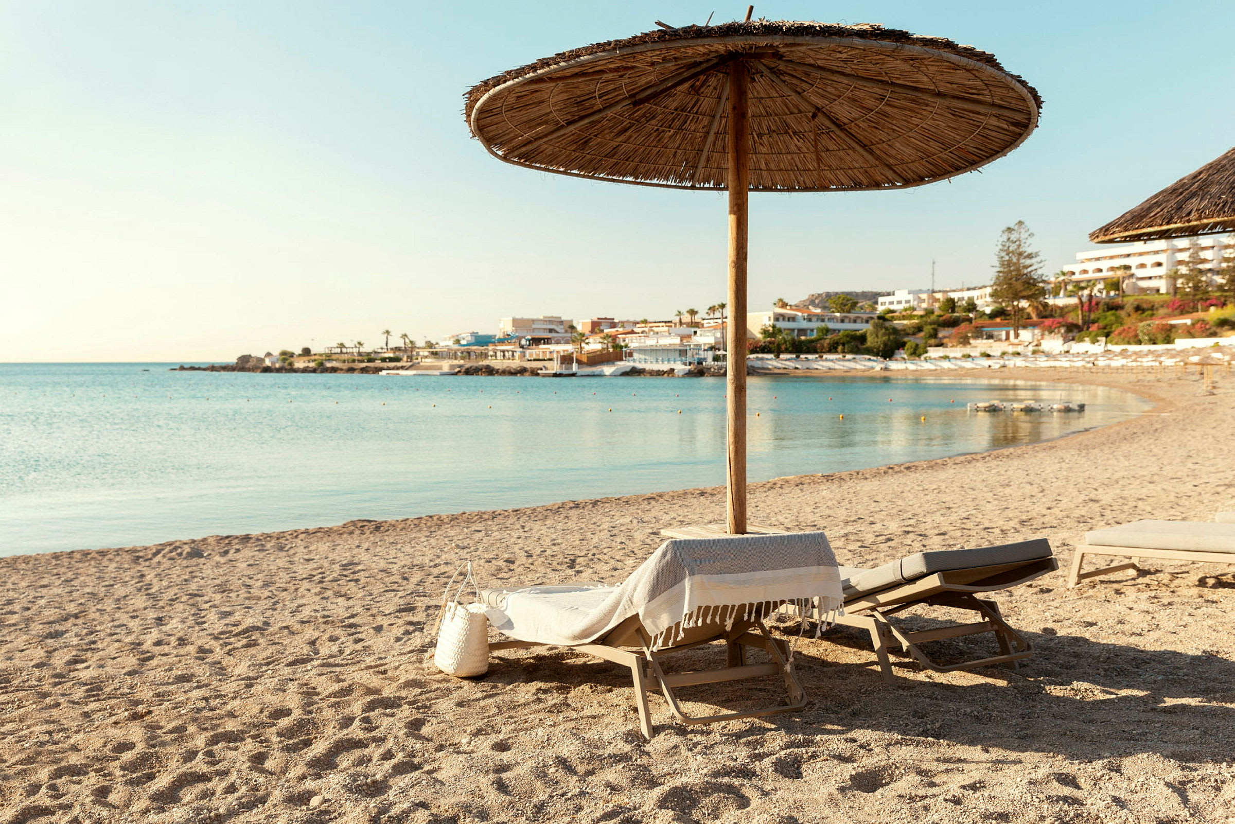 En strand med solstolar och parasoll. Havet och byggnader syns i bakgrunden. (AI-genererad text)