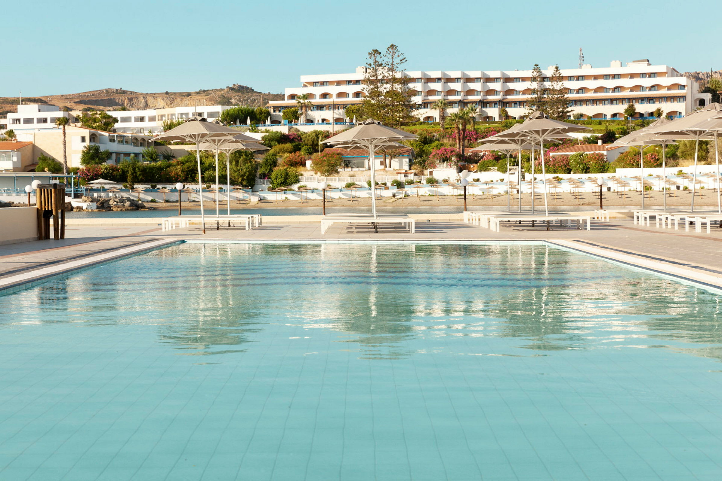 Stor pool med parasoller och hotellbyggnader i bakgrunden. (AI-genererad text)