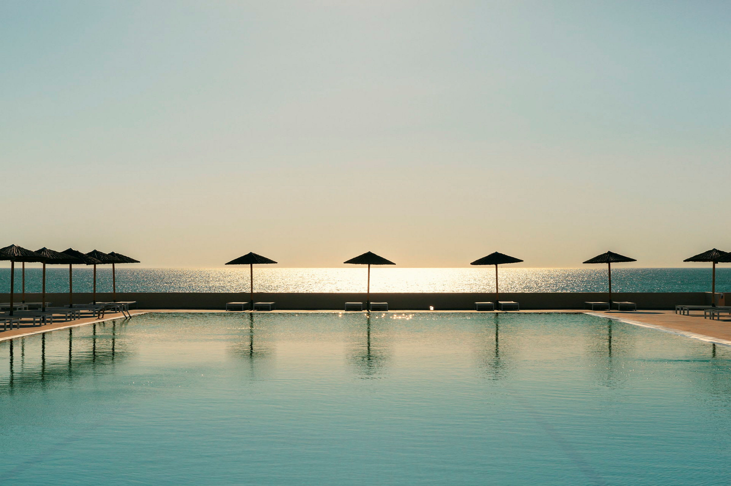 En pool med parasoller framför havet vid solnedgång. (AI-genererad text)