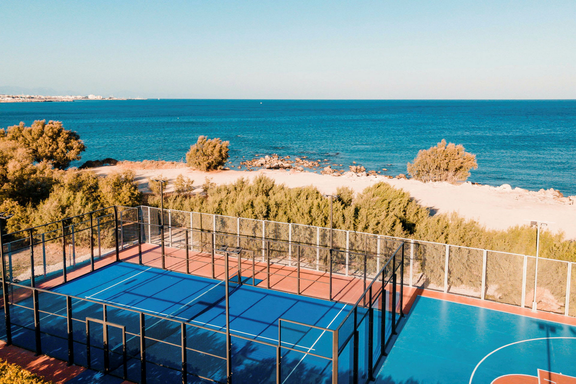 Padelbana med blått underlag nära stranden och havet. (AI-genererad text)