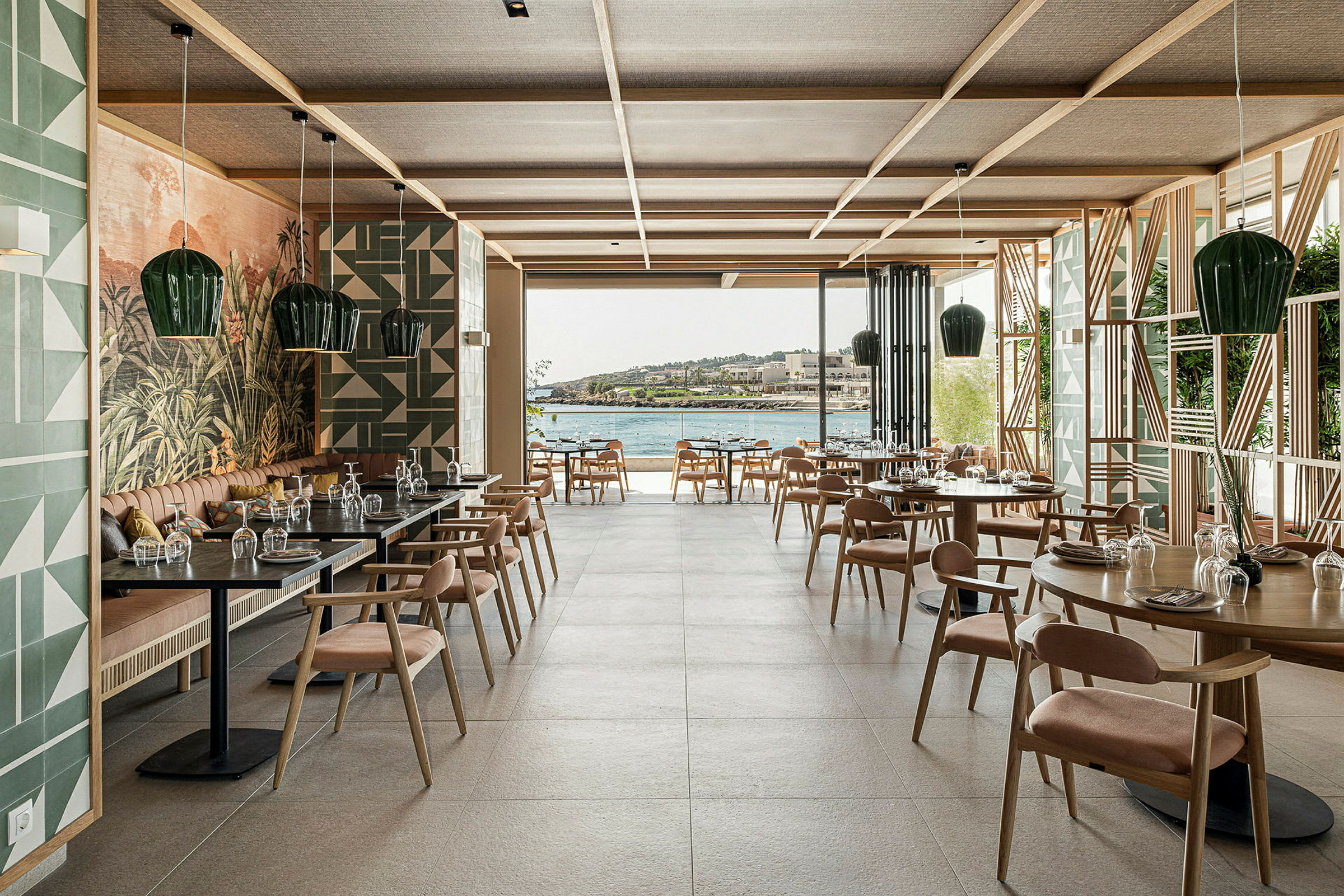 Interiör av en restaurang med bord och stolar, stor glasöppning och utsikt över vattnet. (AI-genererad text)