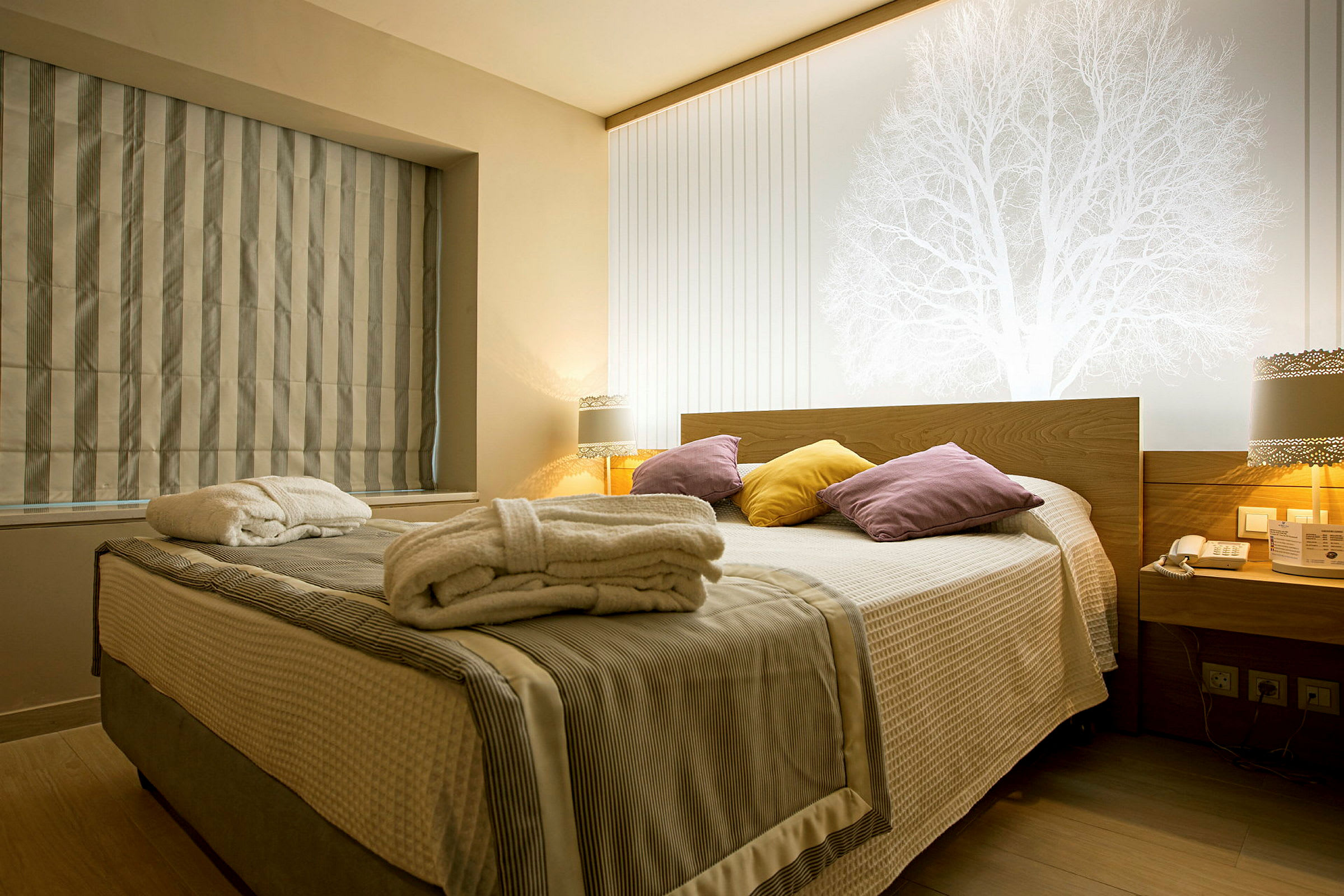 Hotellrum med en dubbelsäng, färgglada kuddar och badrockar på sängen. (AI-genererad text)