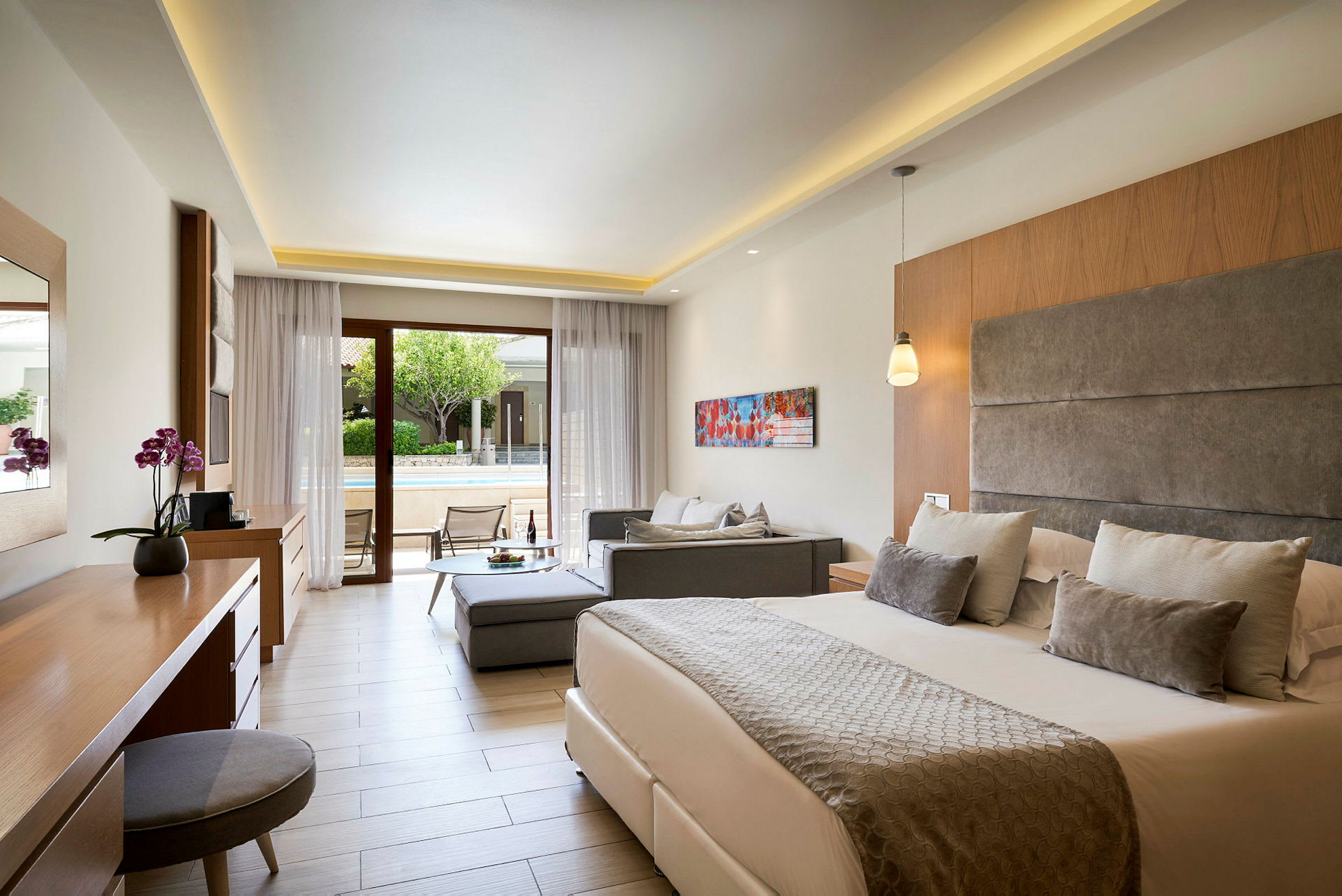 Ett elegant hotellrum med dubbelsäng, soffa och utgång till terrass med solstolar. (AI-genererad text)