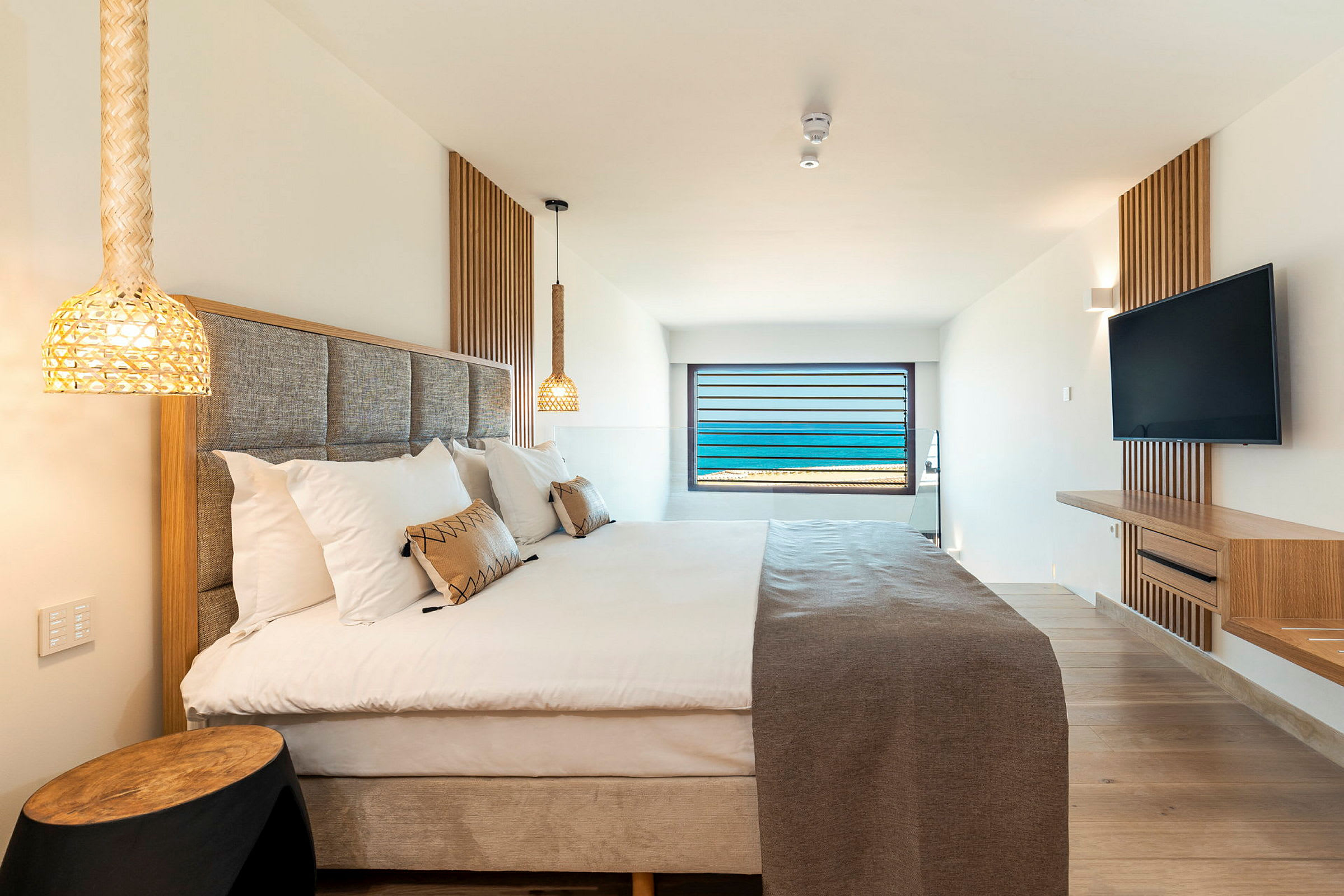 Hotellrum med säng, sänglampor och en väggmonterad TV. Ett fönster med havsutsikt finns längst bort. (AI-genererad text)