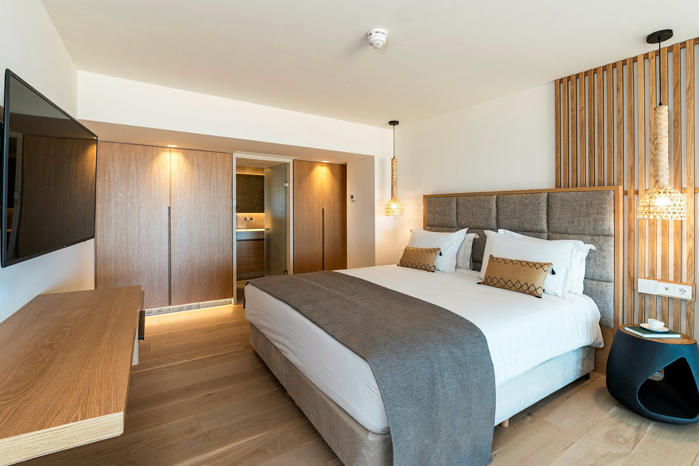 Ett modernt hotellrum med en dubbelsäng, en väggmonterad TV, en träpanel bakom sängen och ett skrivbord. (AI-genererad text)