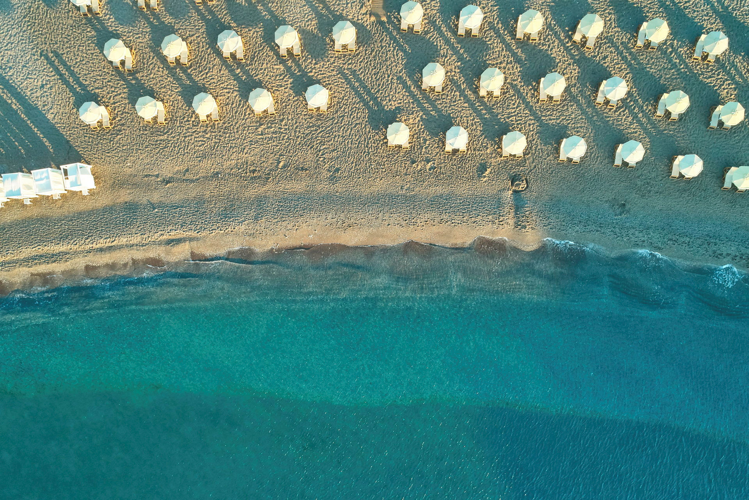 Flygfoto över en strand med parasoller och solstolar, samt klarblått hav. (AI-genererad text)