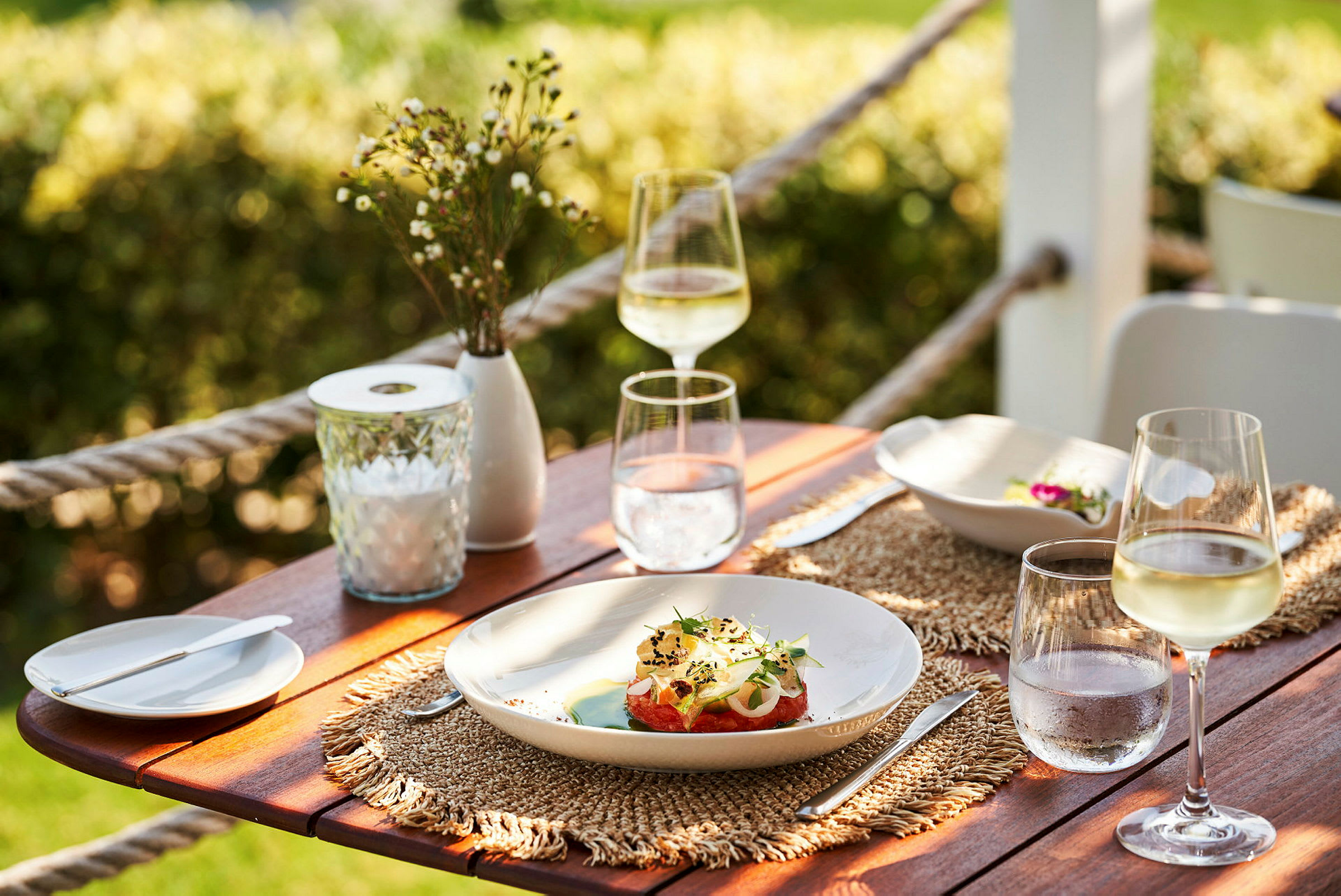 En uppdukad bord vid en utomhusmiljö med tallrikar och glas. (AI-genererad text)