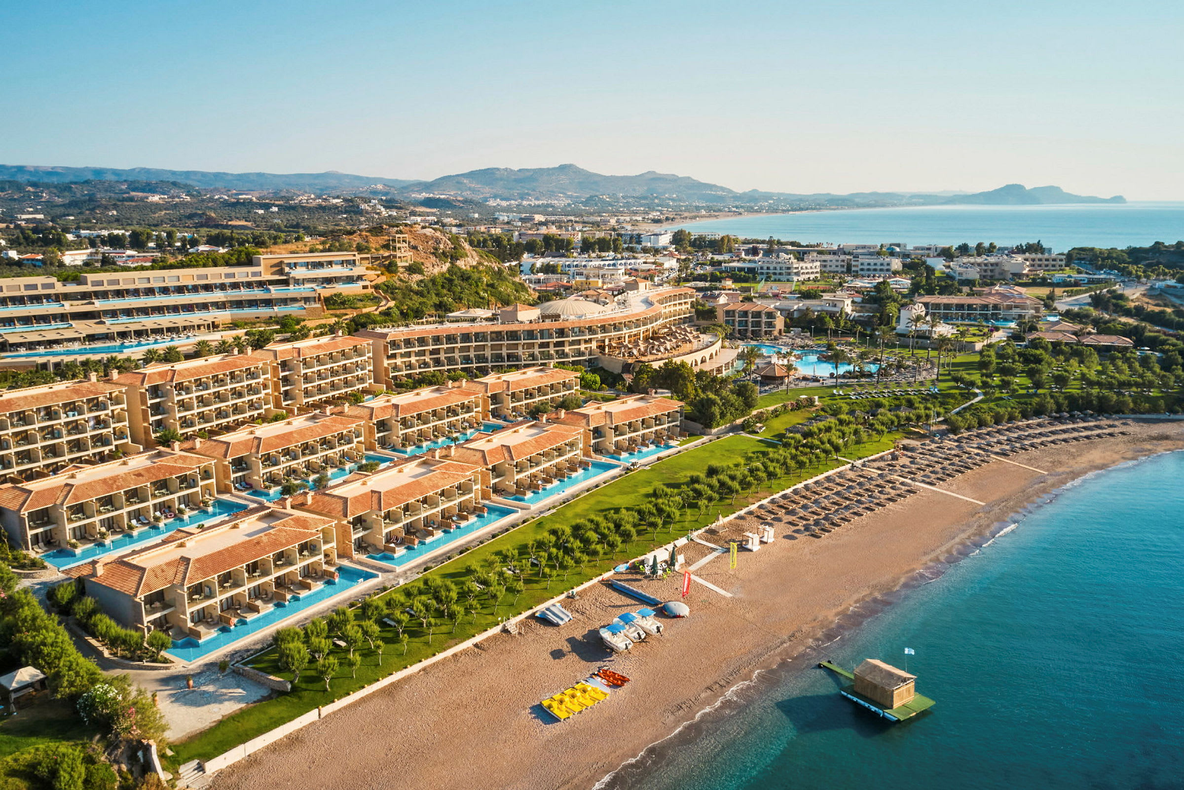 Flygfoto av ett hotellkomplex med pooler och en strand i förgrunden. (AI-genererad text)