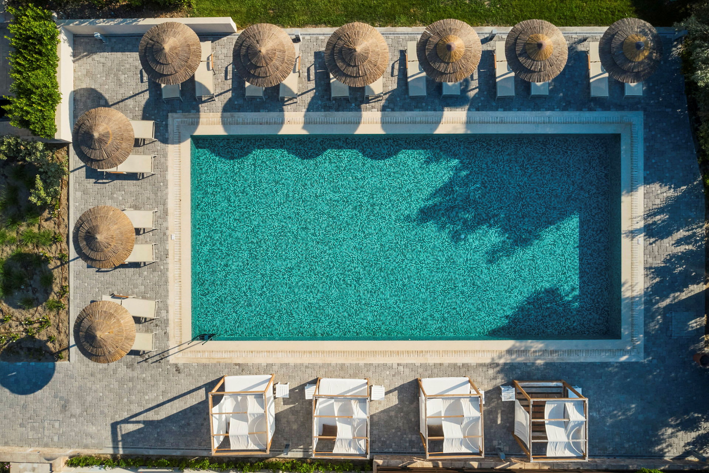 Flygbild på en rektangulär pool omgiven av parasoller och solstolar. (AI-genererad text)