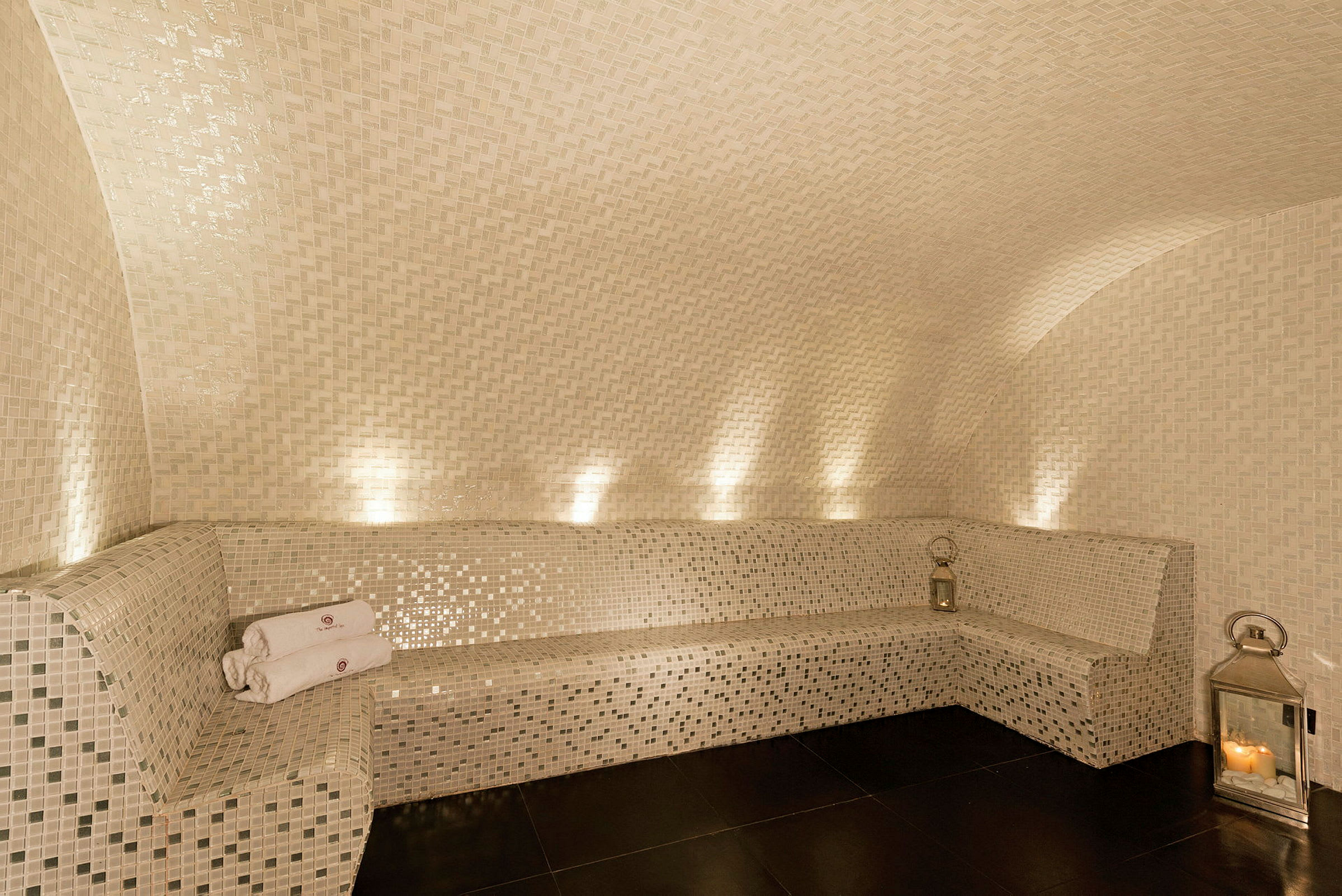 Mosaikklädda väggar och bänk med ljuslykta och ihopvikta handdukar i ett elegant spaområde. (AI-genererad text)