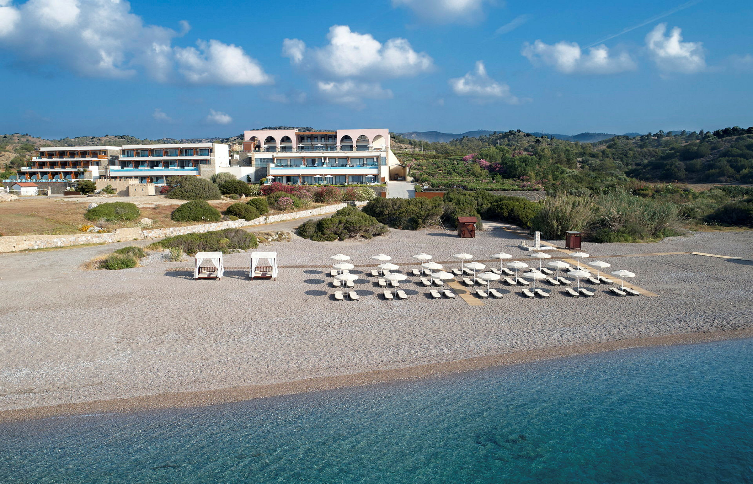 Ett strandhotell med solstolar och parasoller uppställda på en stenstrand nära klart blått vatten. (AI-genererad text)