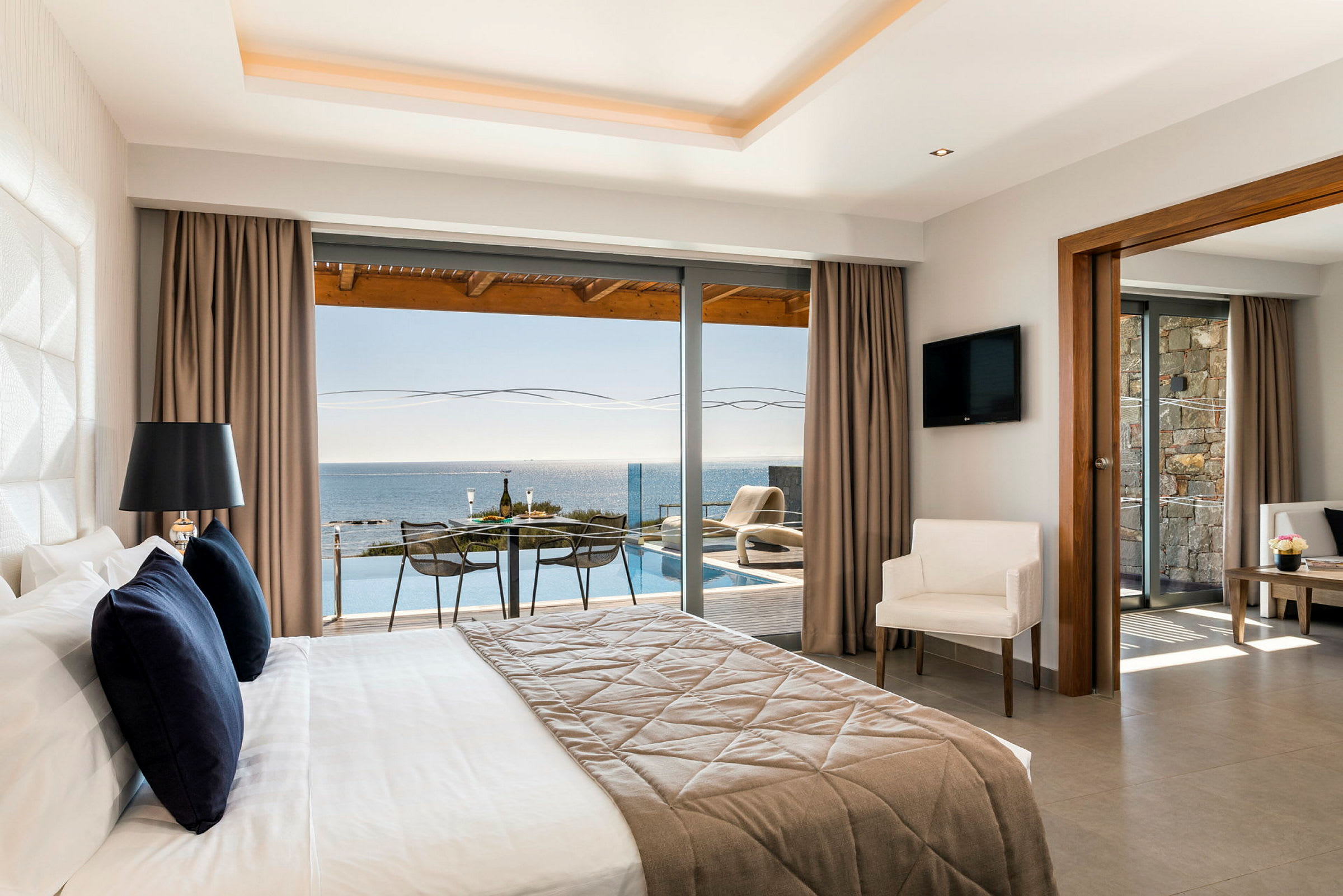 Ett hotellrum med stor säng och utsikt mot havet från ett glasparti. (AI-genererad text)