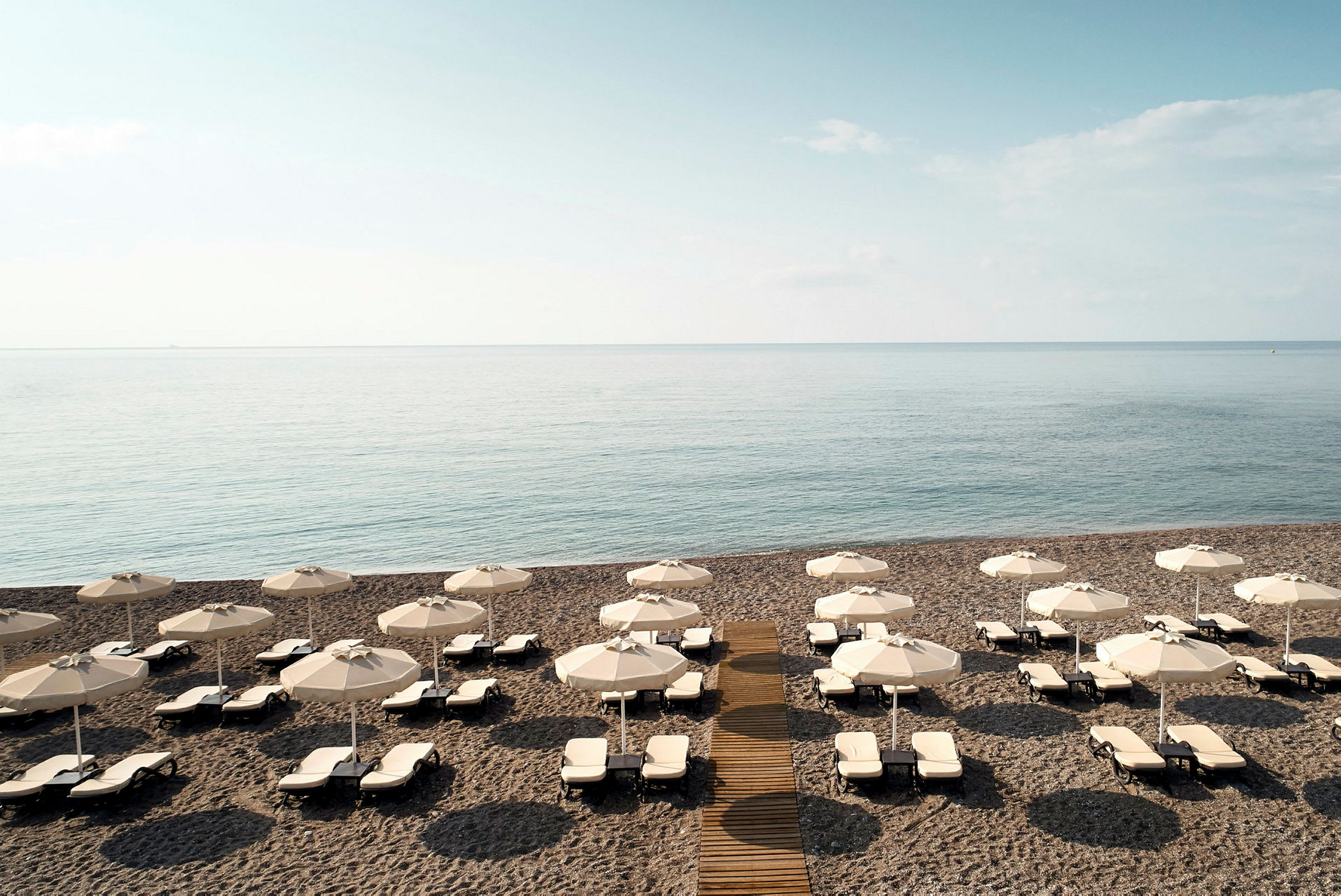 Strand med solstolar och parasoller, hav i bakgrunden. (AI-genererad text)