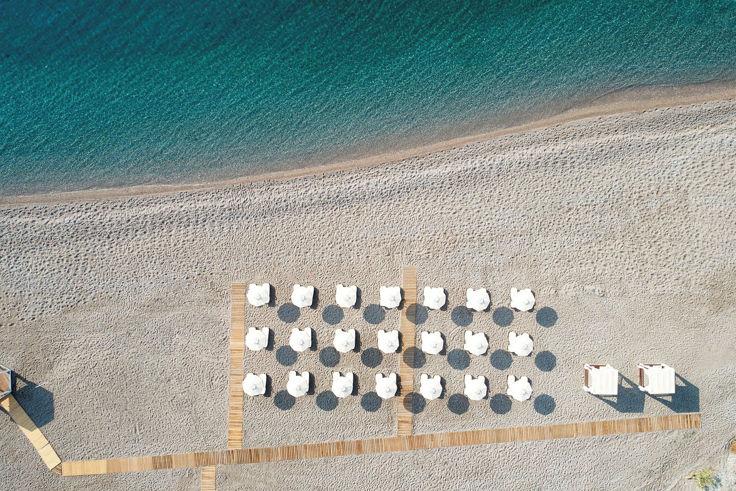 Strand med vita parasoller och solstolar på sanden sedd ovanifrån. (AI-genererad text)