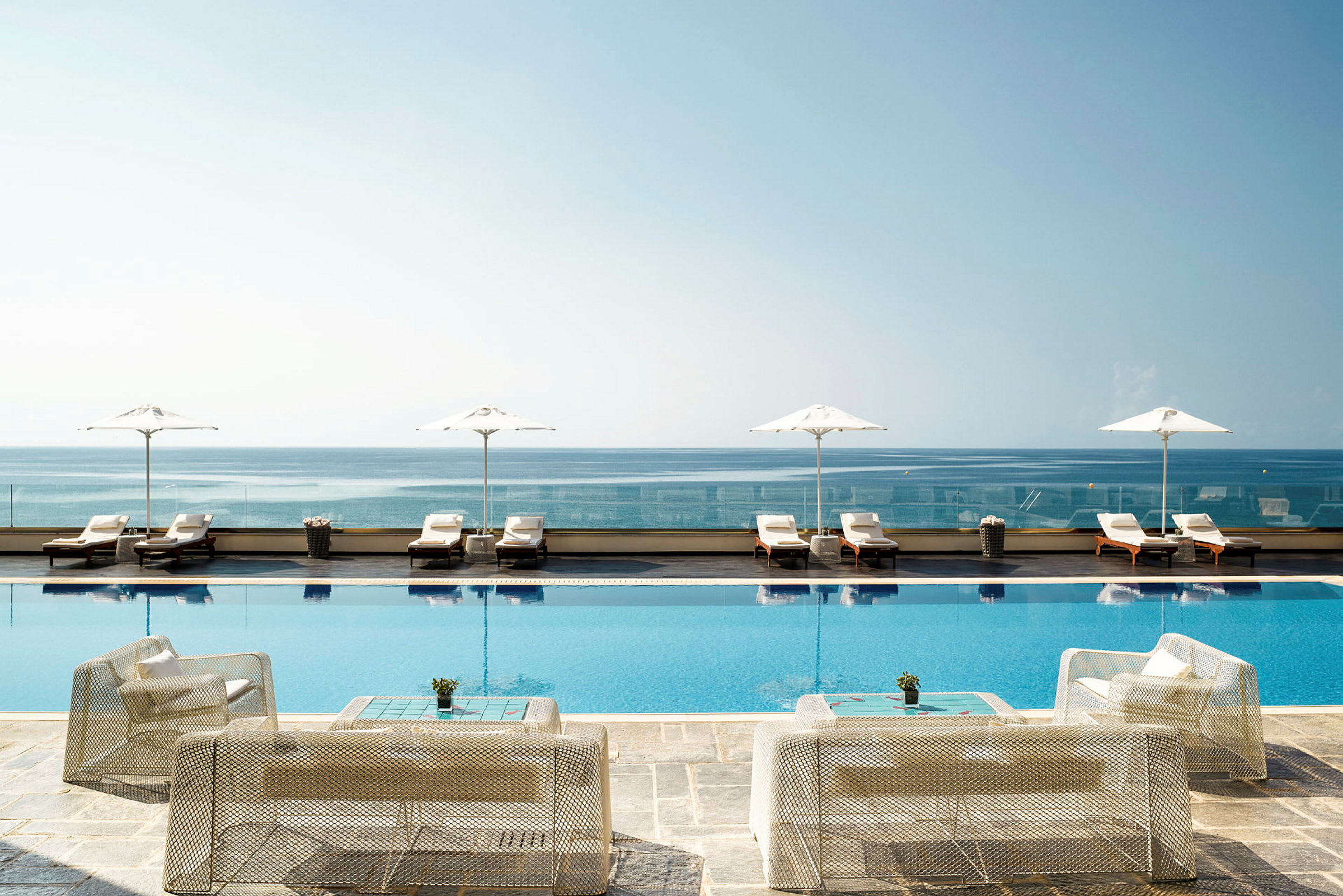 Bild av en infinitypool vid kusten, med solstolar och parasoller i bakgrunden. (AI-genererad text)
