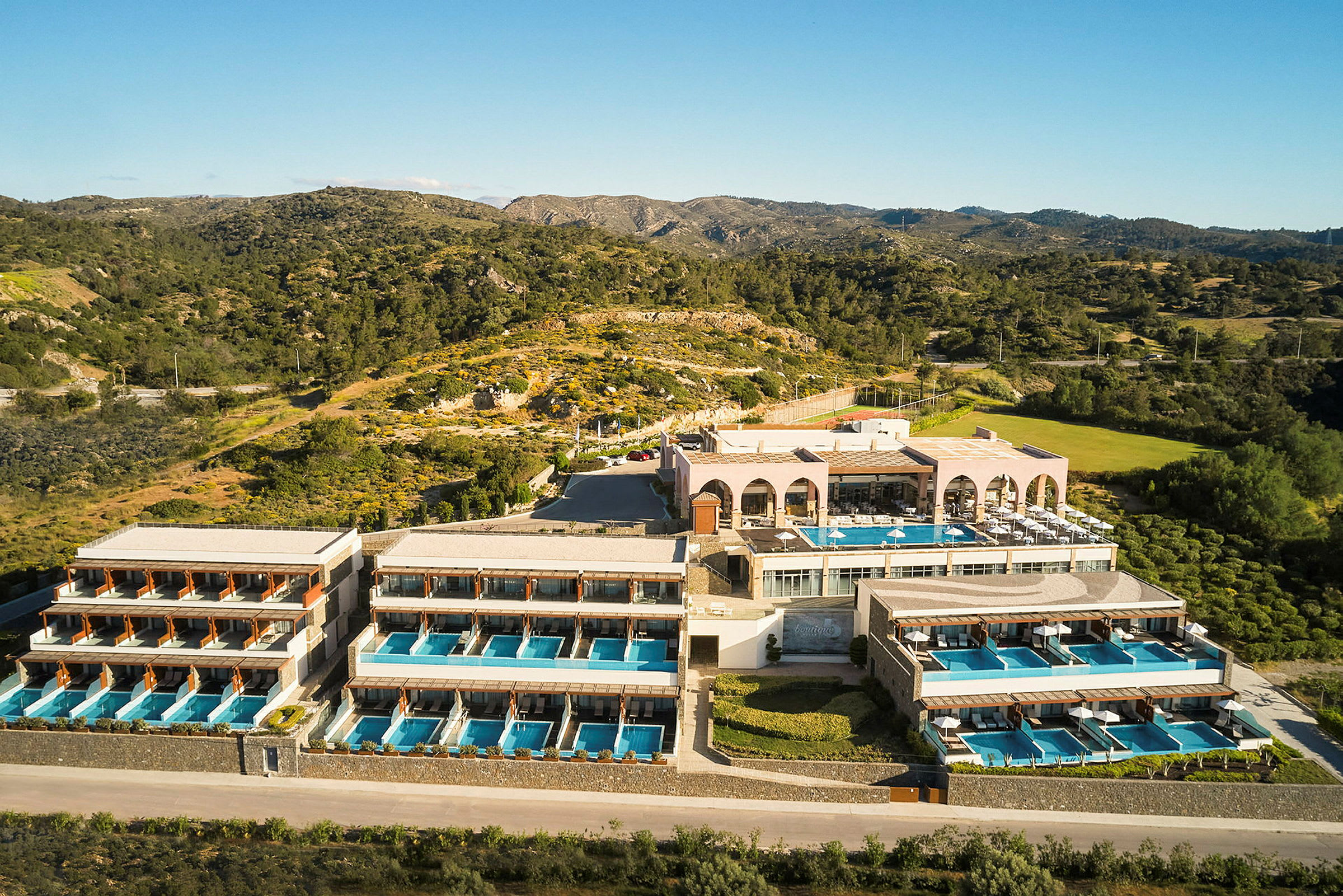 Hotellkomplex med flera byggnader och privata pooler, beläget i naturligt landskap med berg och vegetation. (AI-genererad text)