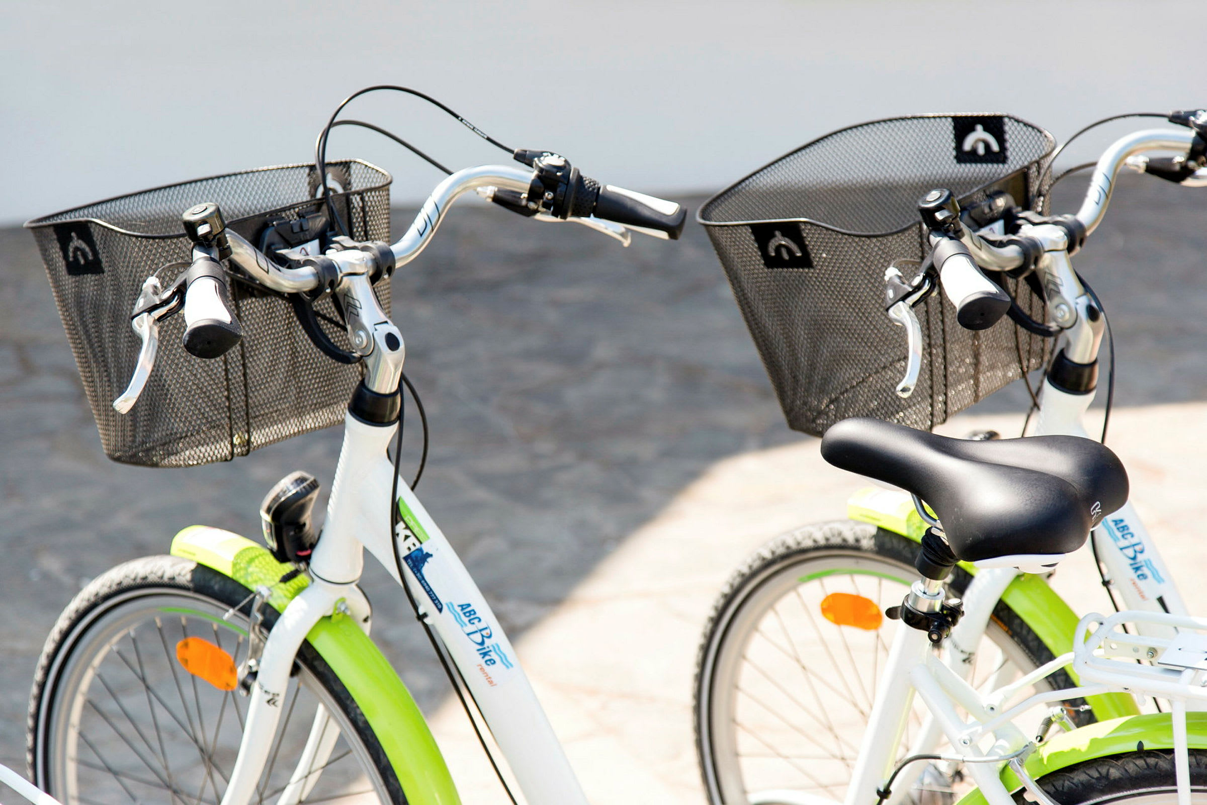 Två vita cyklar med svarta sadlar och korgar visas. (AI-genererad text)