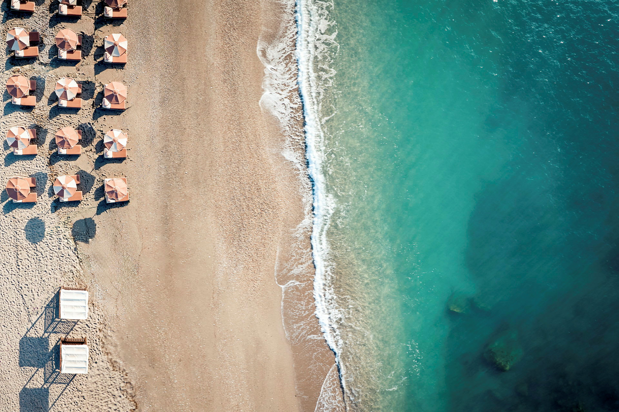 Flygfoto av en strand med parasoller och turkost vatten. (AI-genererad text)