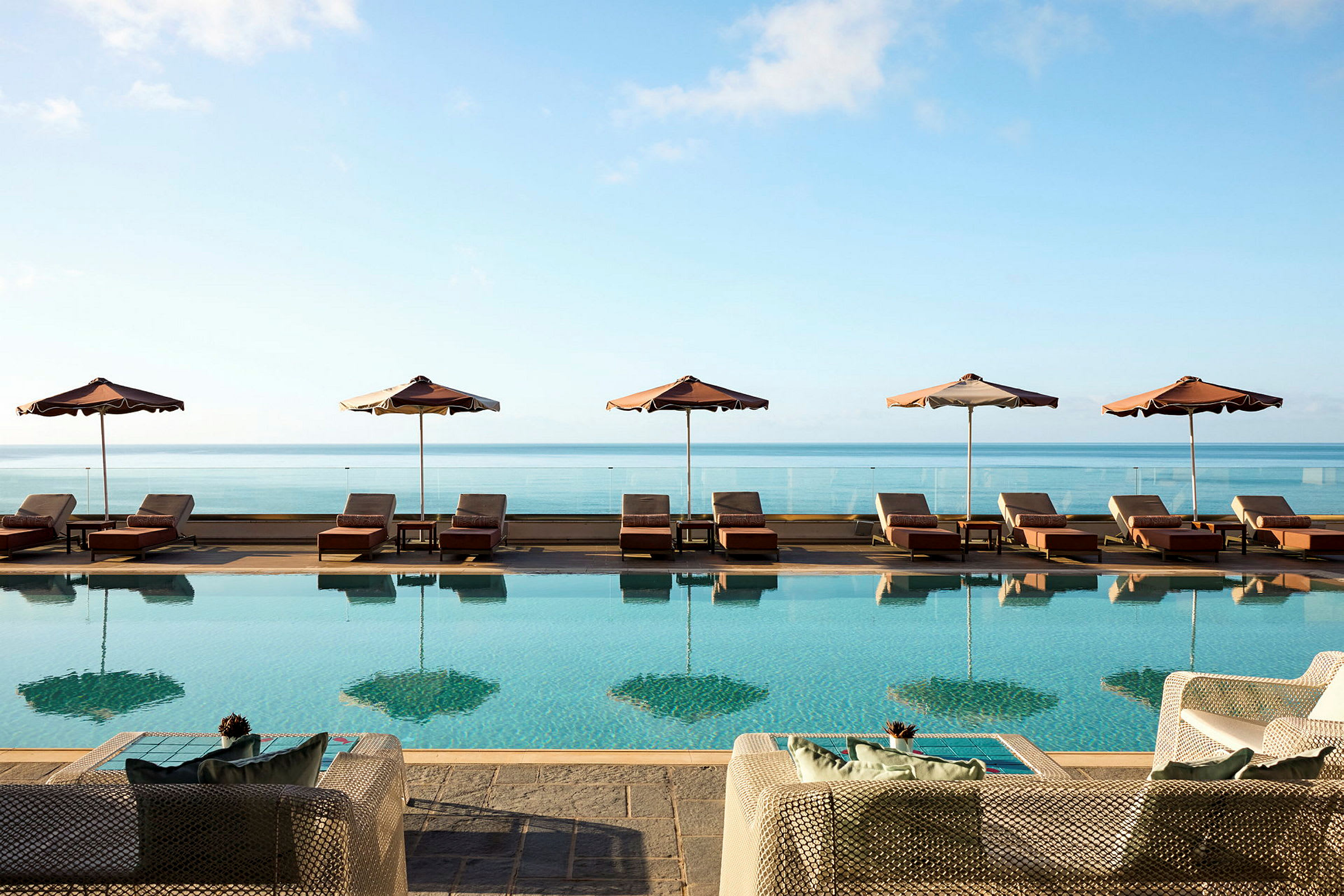 Bild av en pool med solstolar och parasoller. Utsikt mot havet under en klarblå himmel. (AI-genererad text)