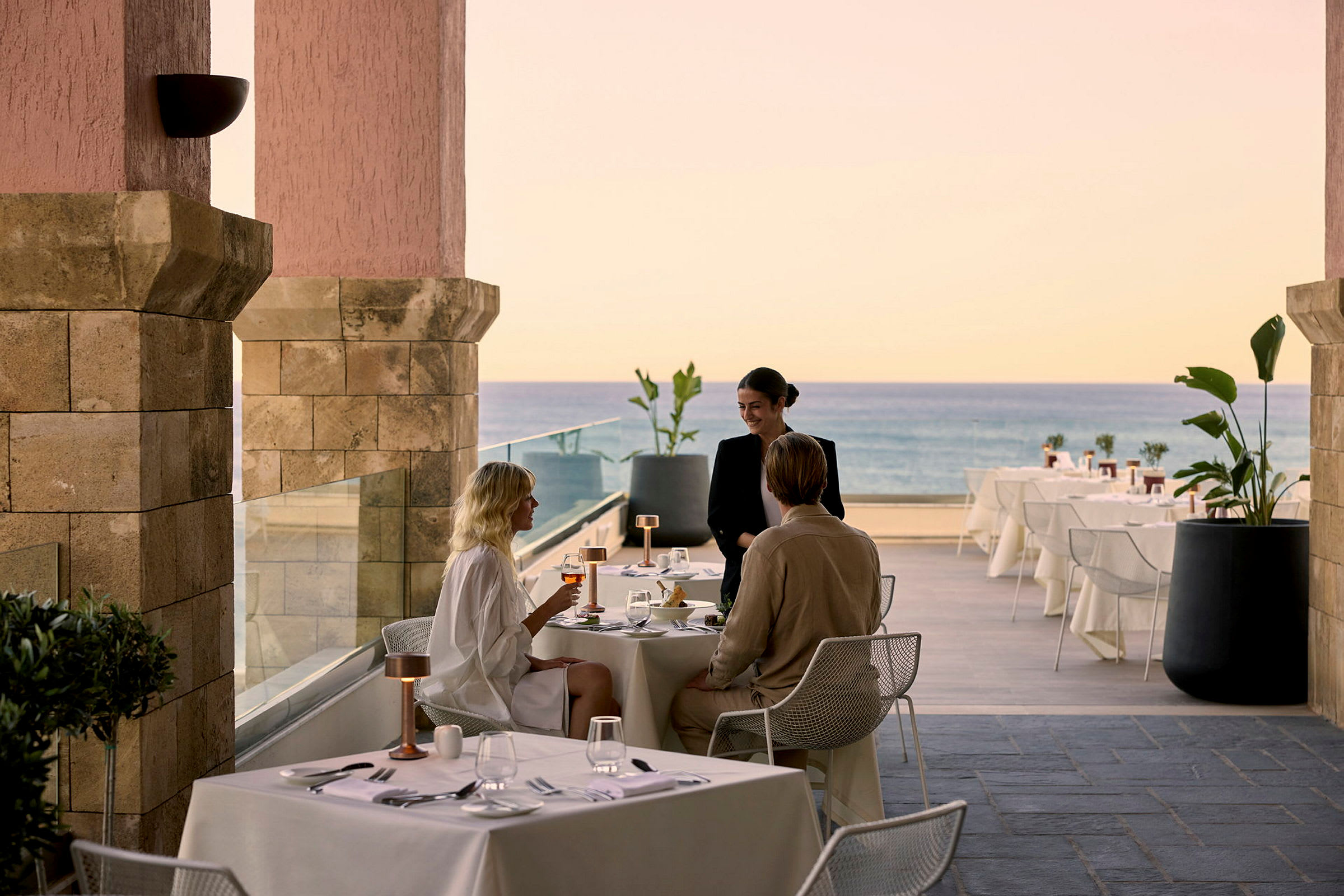 Personer som sitter vid ett dukat restaurangbord med utsikt över havet. (AI-genererad text)