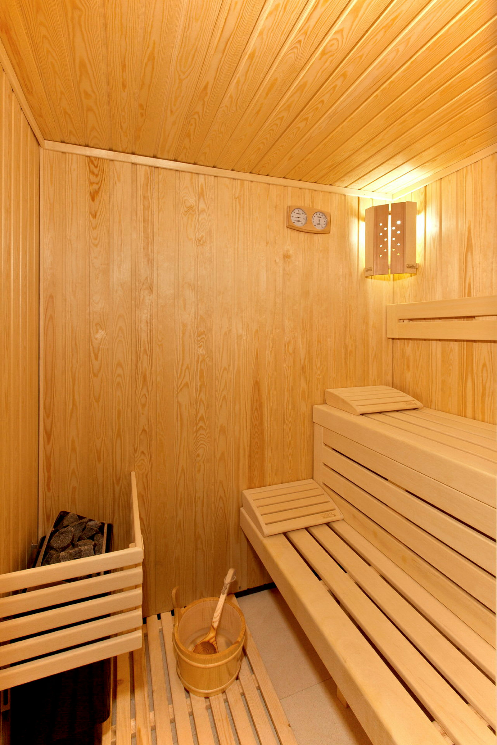 Bild av en interiör av en träbaserad sauna med sittbänkar och en hink med vattenskopa. (AI-genererad text)