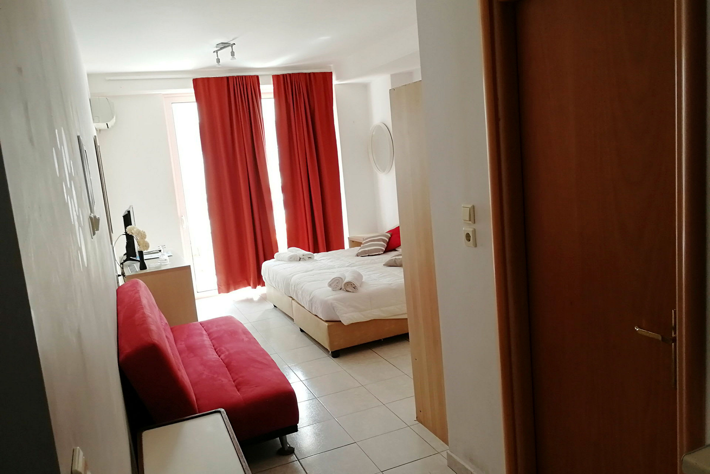 Ett hotellrum med en bäddad säng, röda gardiner och en röd soffa. (AI-genererad text)