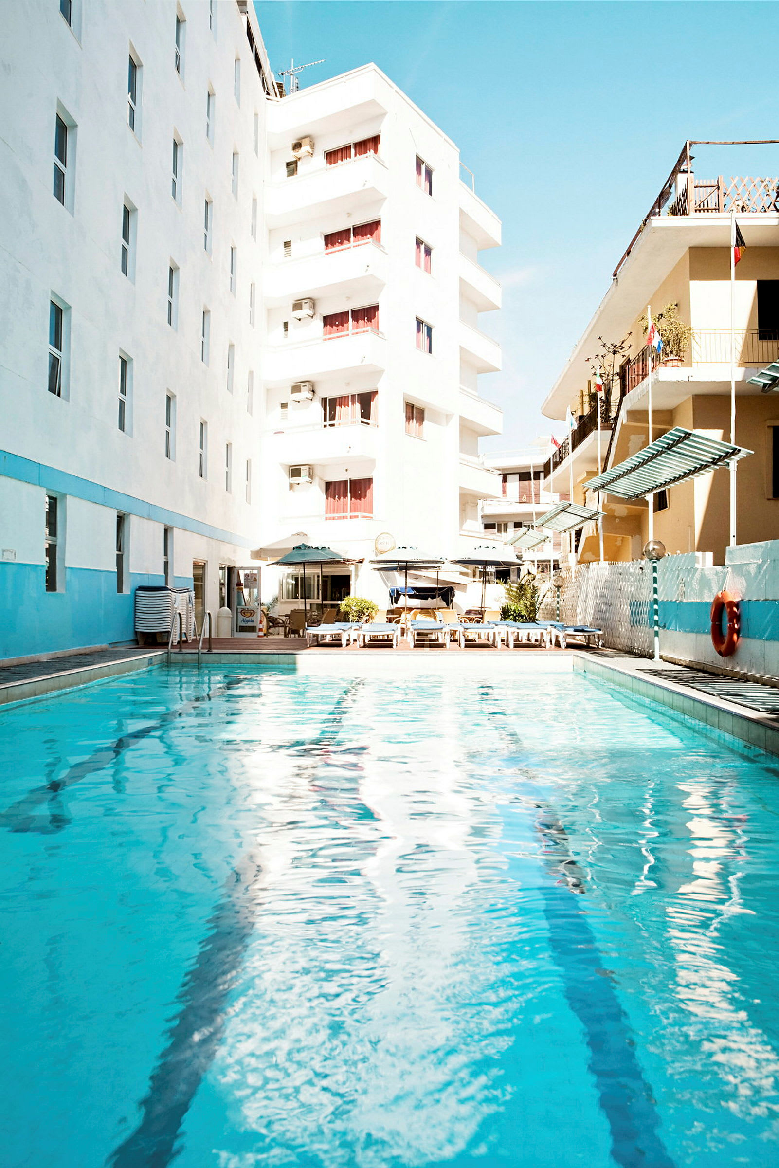 En utomhuspool omgiven av hotellbyggnader och solstolar. (AI-genererad text)