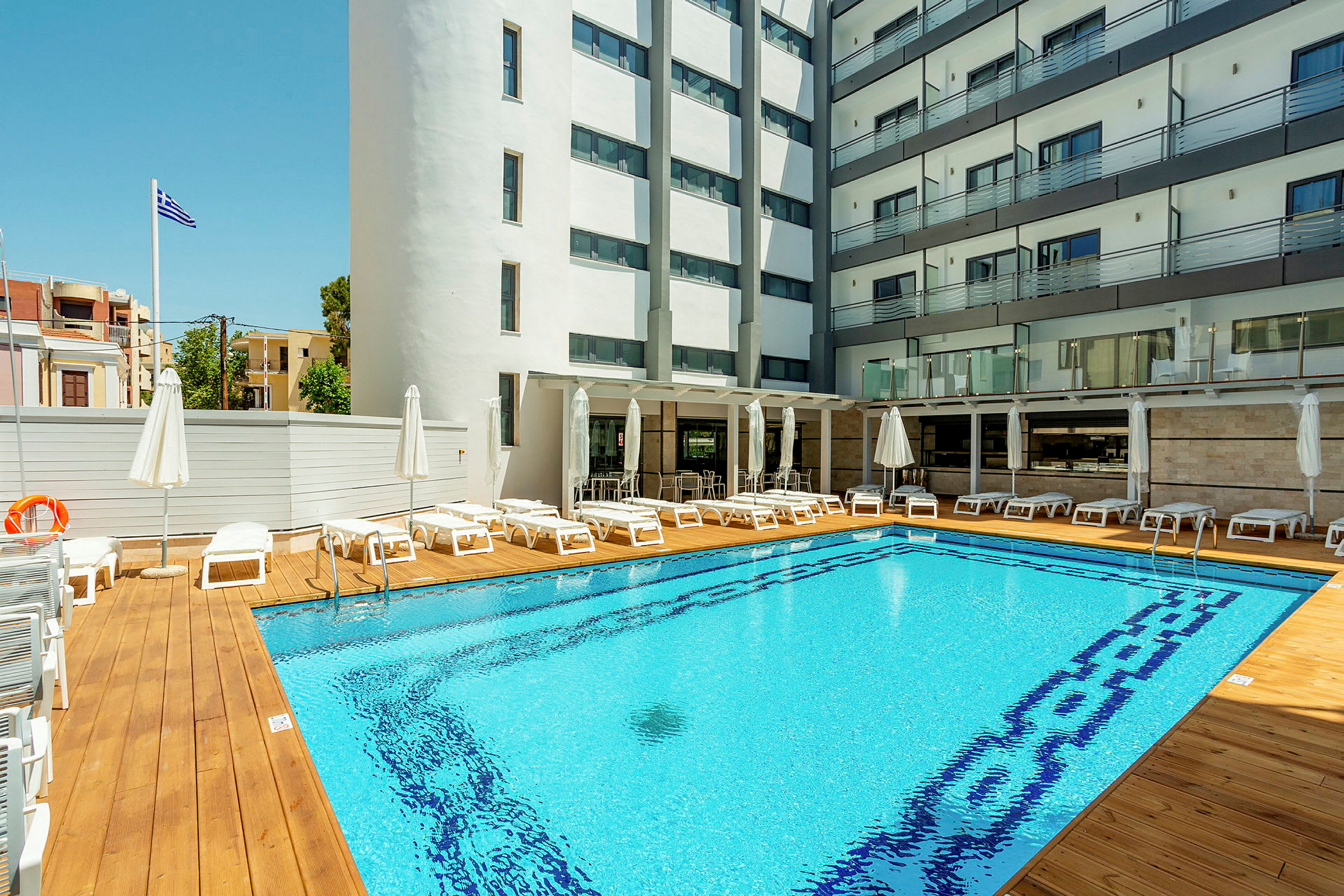 Hotellpool med solstolar och parasoller, omgiven av byggnader. (AI-genererad text)