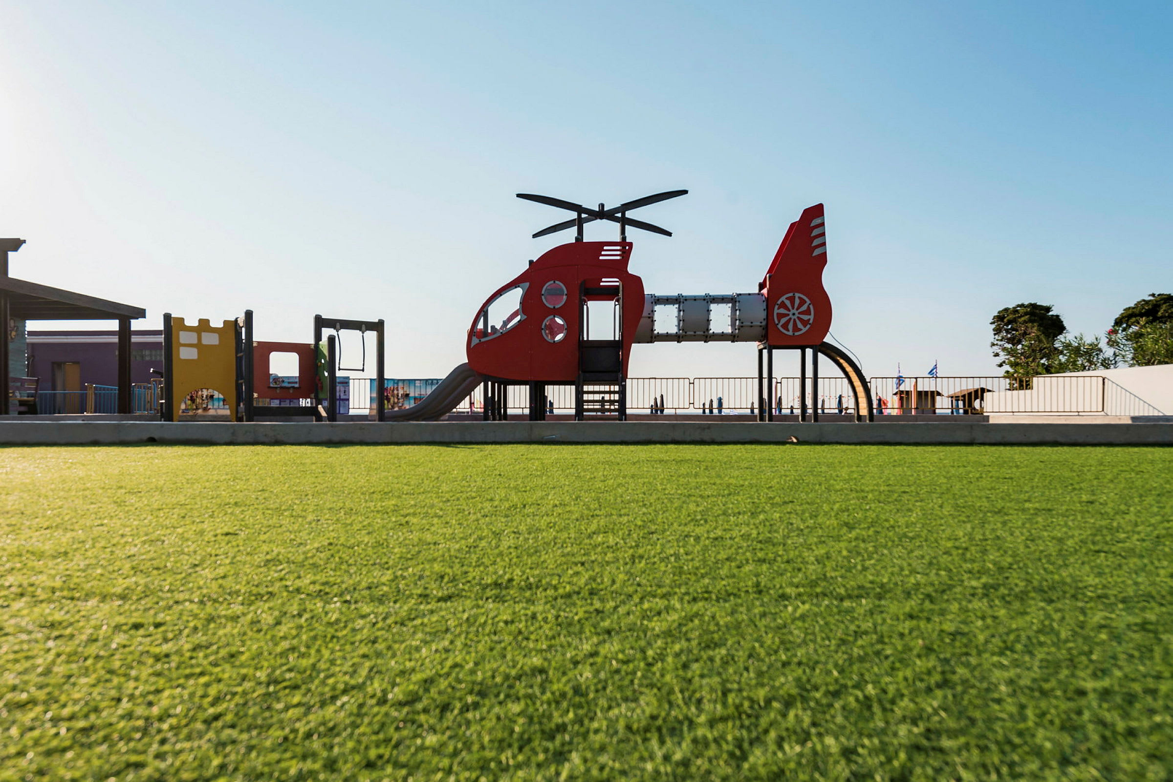 Lekplats med helikopterformade lekstrukturer och grönskande gräsmatta. (AI-genererad text)