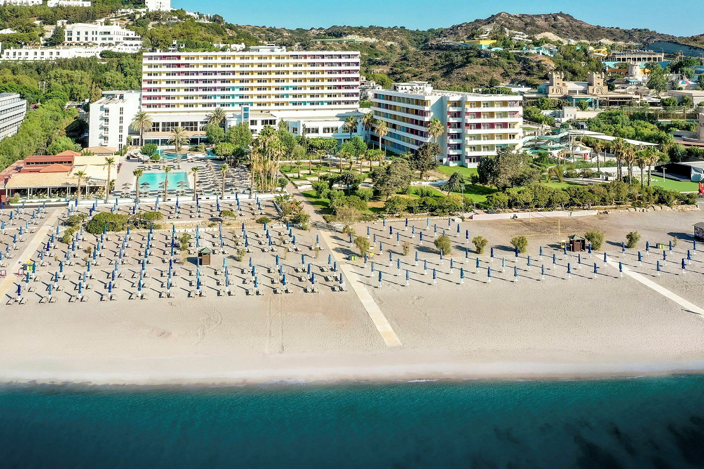 Hotellkomplex vid stranden med solstolar och parasoller, och havet i förgrunden. (AI-genererad text)