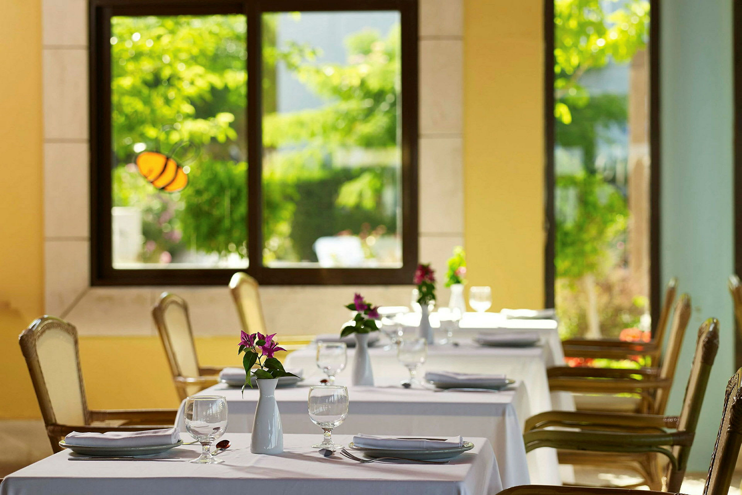 Restaurang med dukade bord och blommor i en ljus miljö. (AI-genererad text)