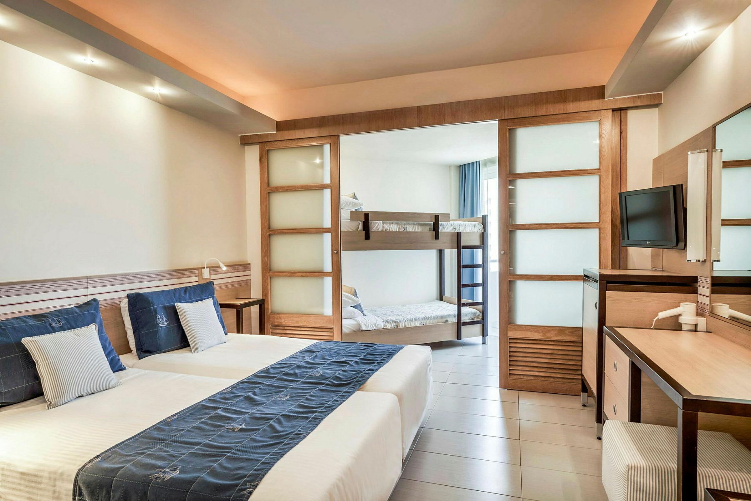 Ett hotellrum med två dubbelsängar, våningssängar i bakgrunden och en skrivbordsplats. (AI-genererad text)