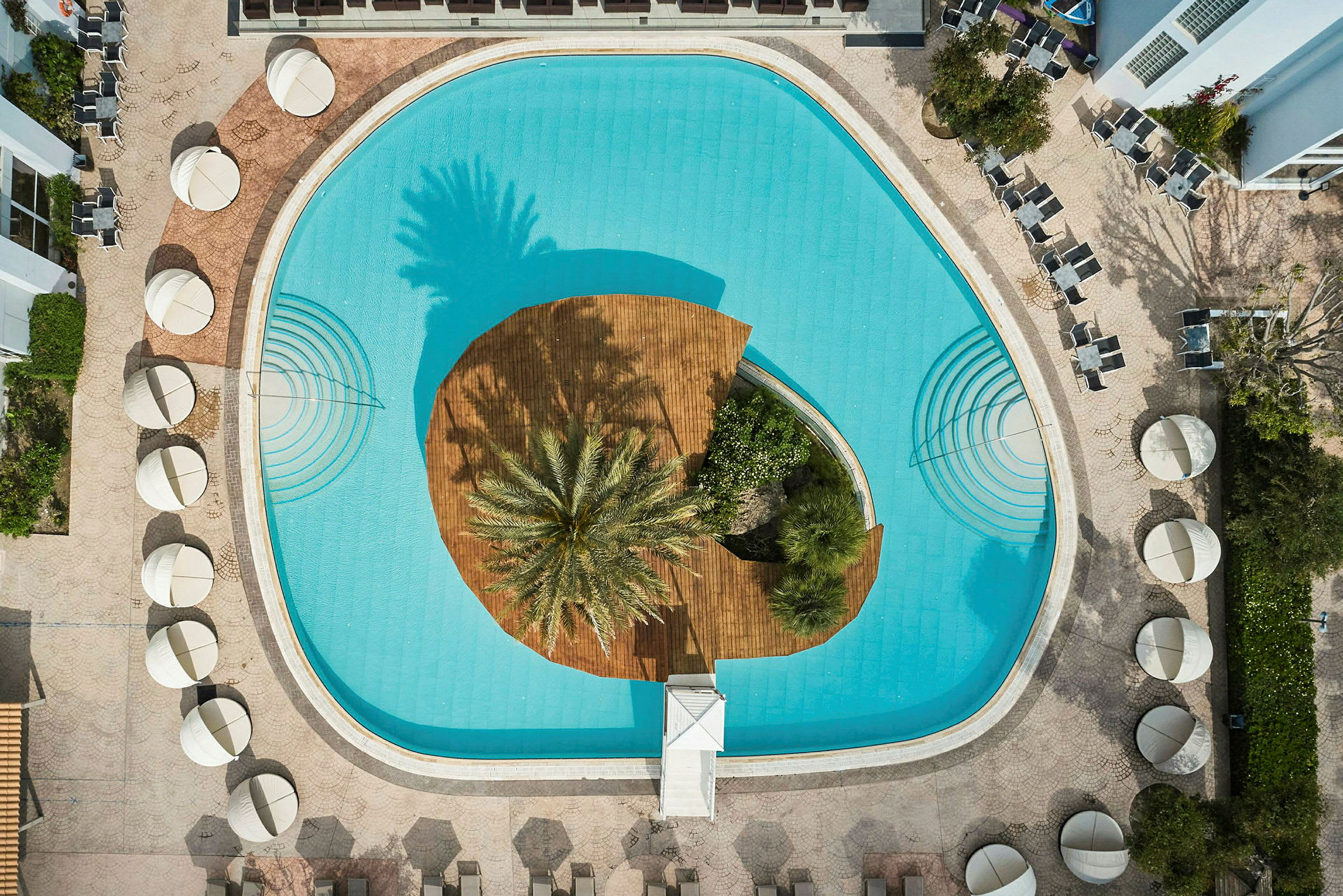 En pool med en central ö av trä och palmträd, sedd från ovan. (AI-genererad text)