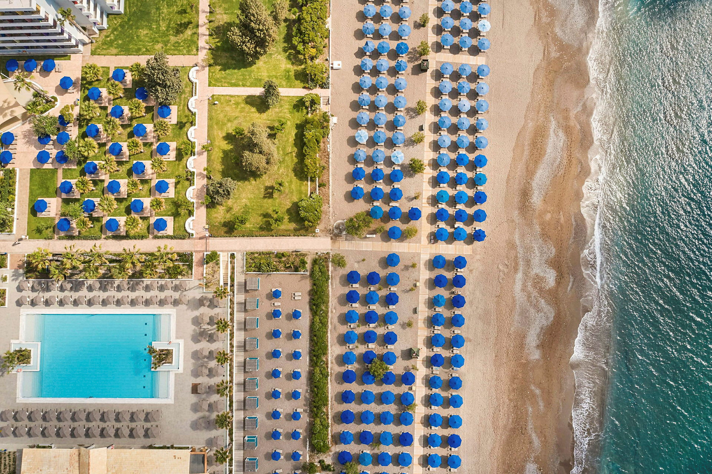 Flygfoto av strand med solparasoller i blått, poolområde och grönska. (AI-genererad text)